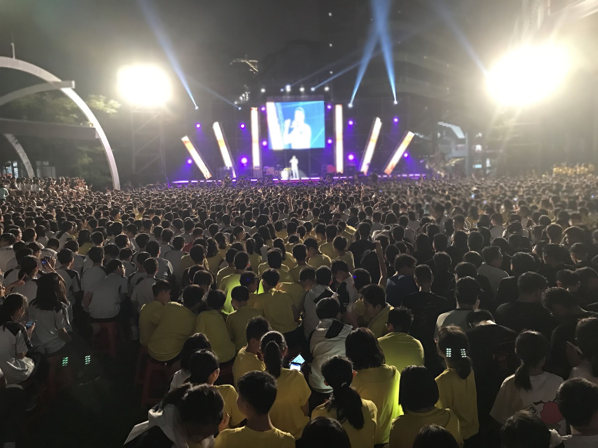 戶外音樂會人山人海，舞檯燈光明亮，螢幕上有歌手。