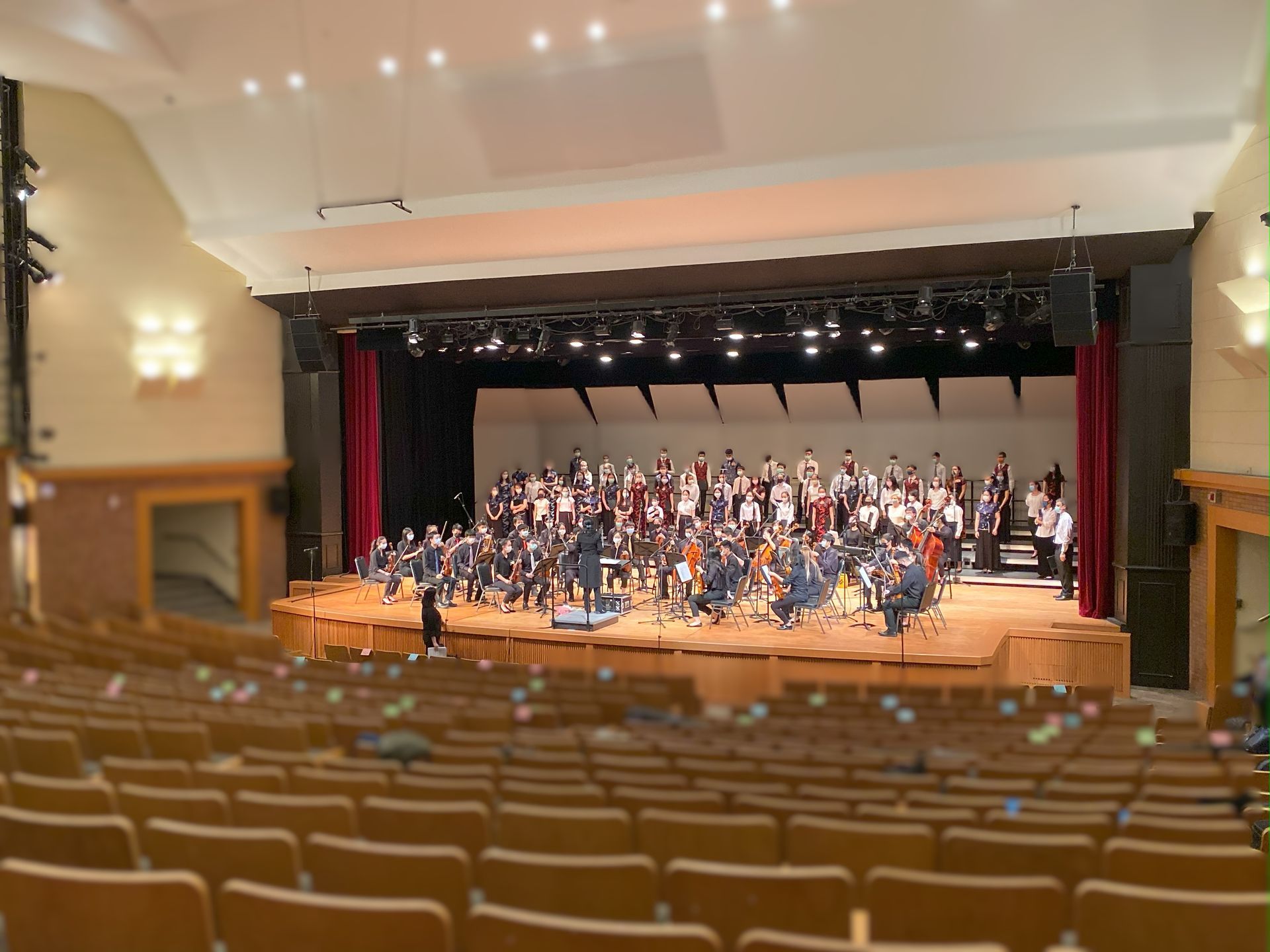 劇院舞台上，管弦樂團和合唱團正在表演。前景是一排排座位。