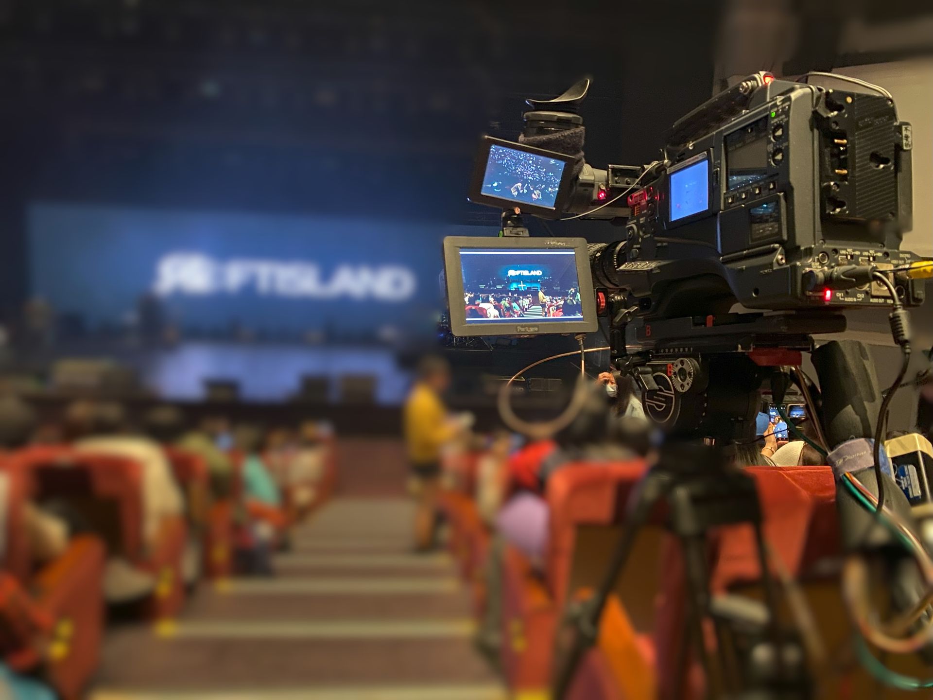 攝影機正在拍攝 FTISLAND 樂團的音樂會；可以看到模糊的觀眾座位。