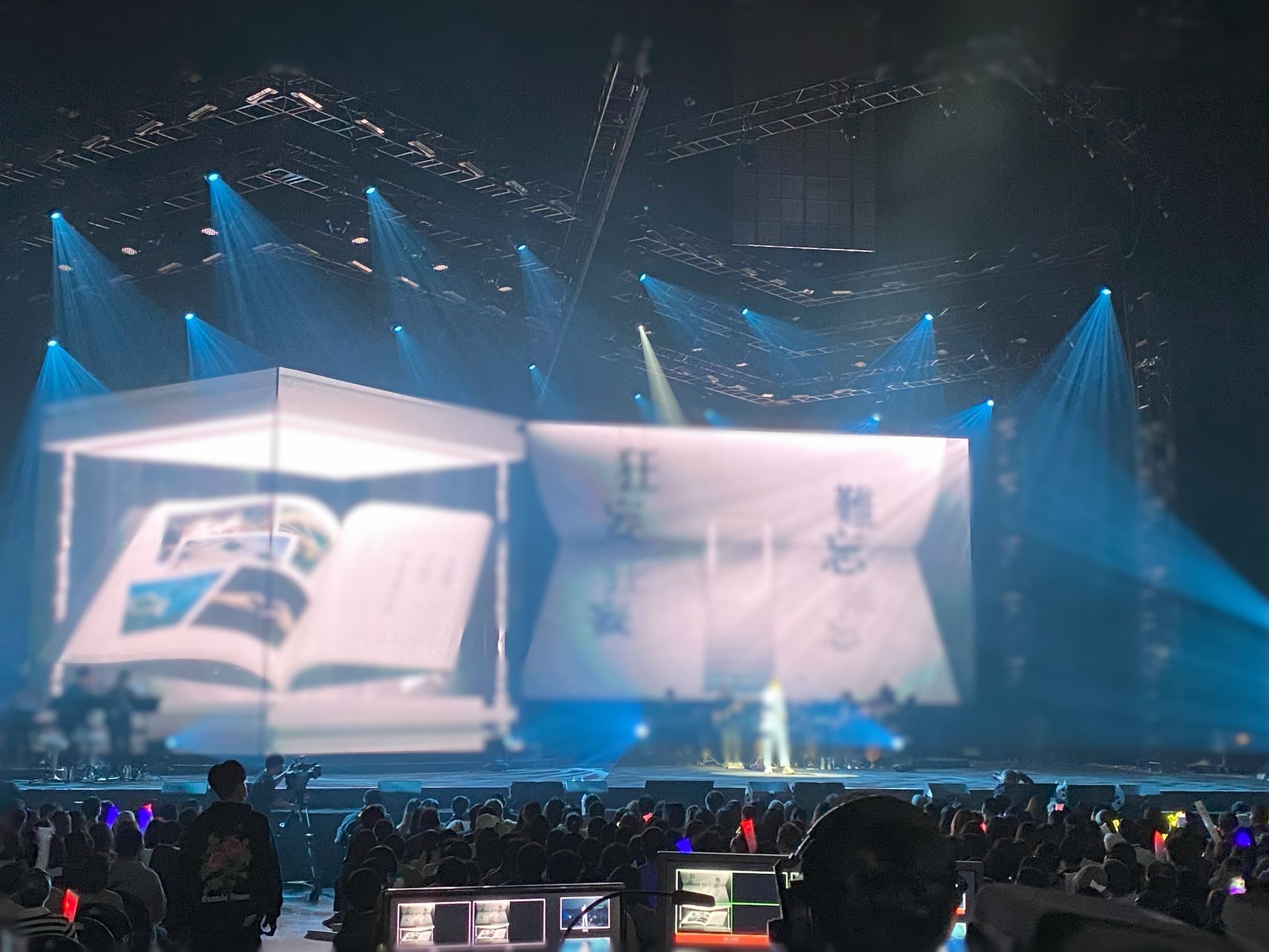 音樂會舞台上有巨幅書籍投影、表演者、觀眾、藍色燈光。