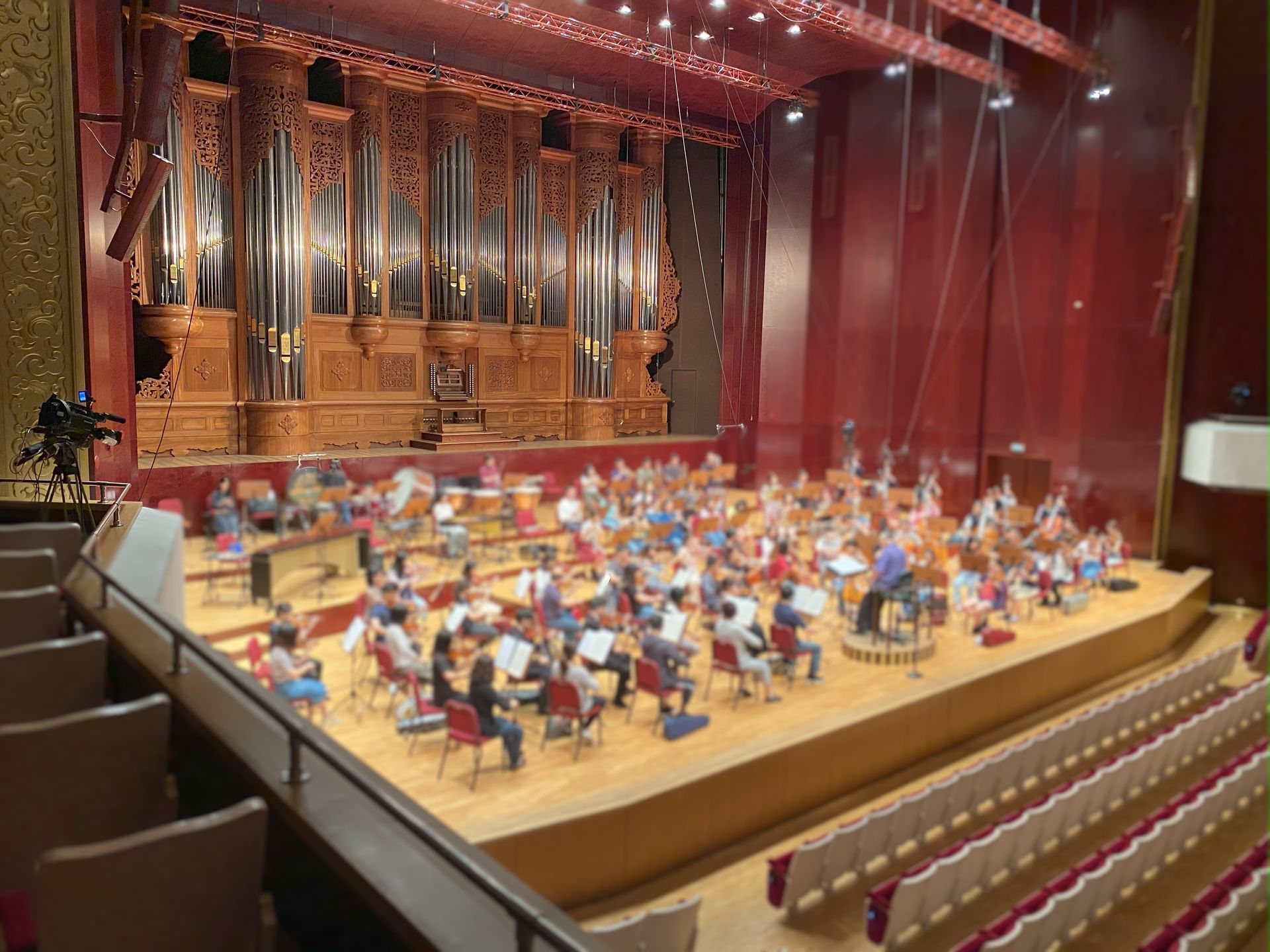 一支管弦樂團在舞台上表演，背景是一架大型管風琴；場景是一座禮堂。