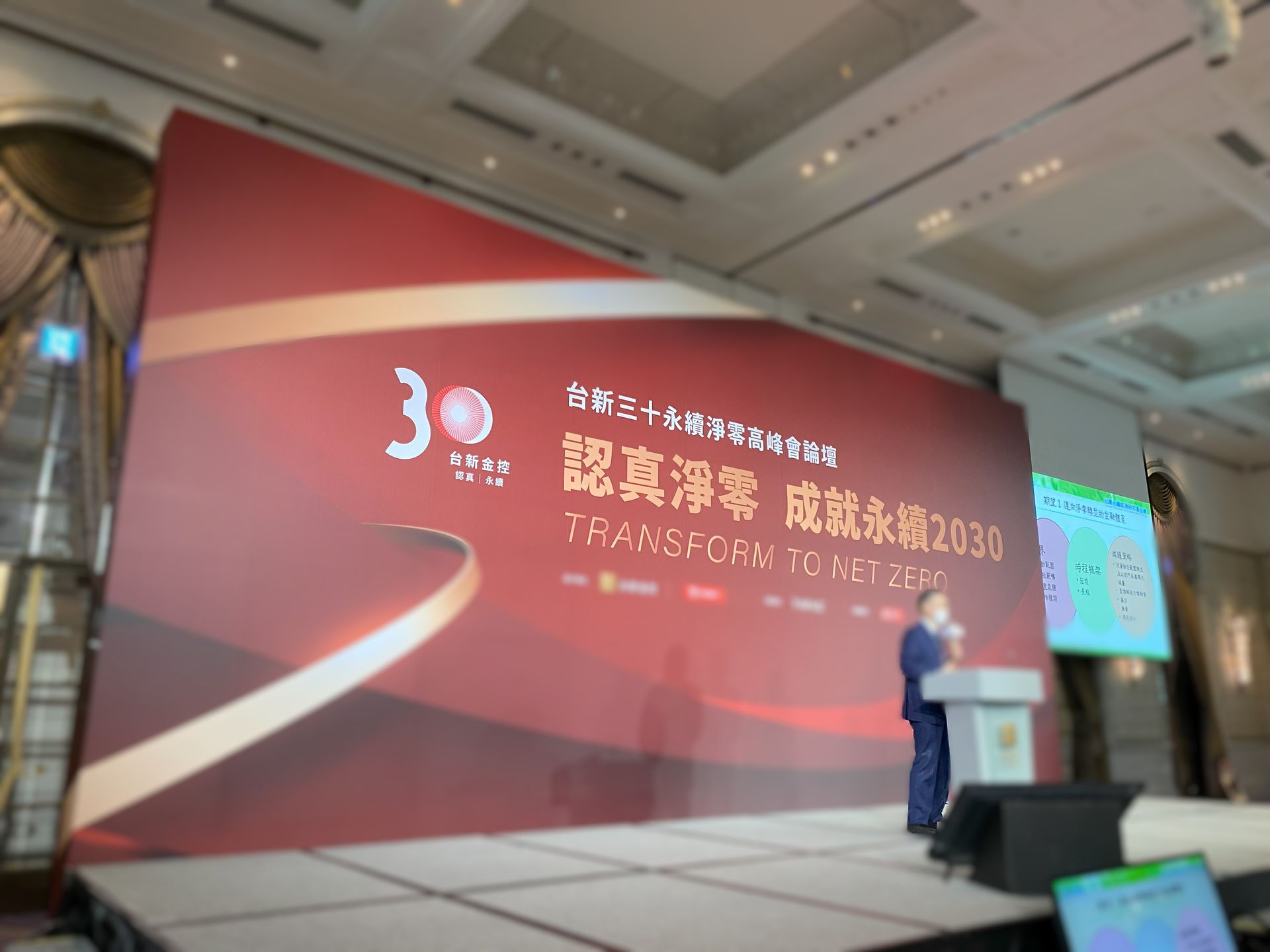 一名男子在會議上發表講話，手持紅色和金色的橫幅；舞台，正式場景。