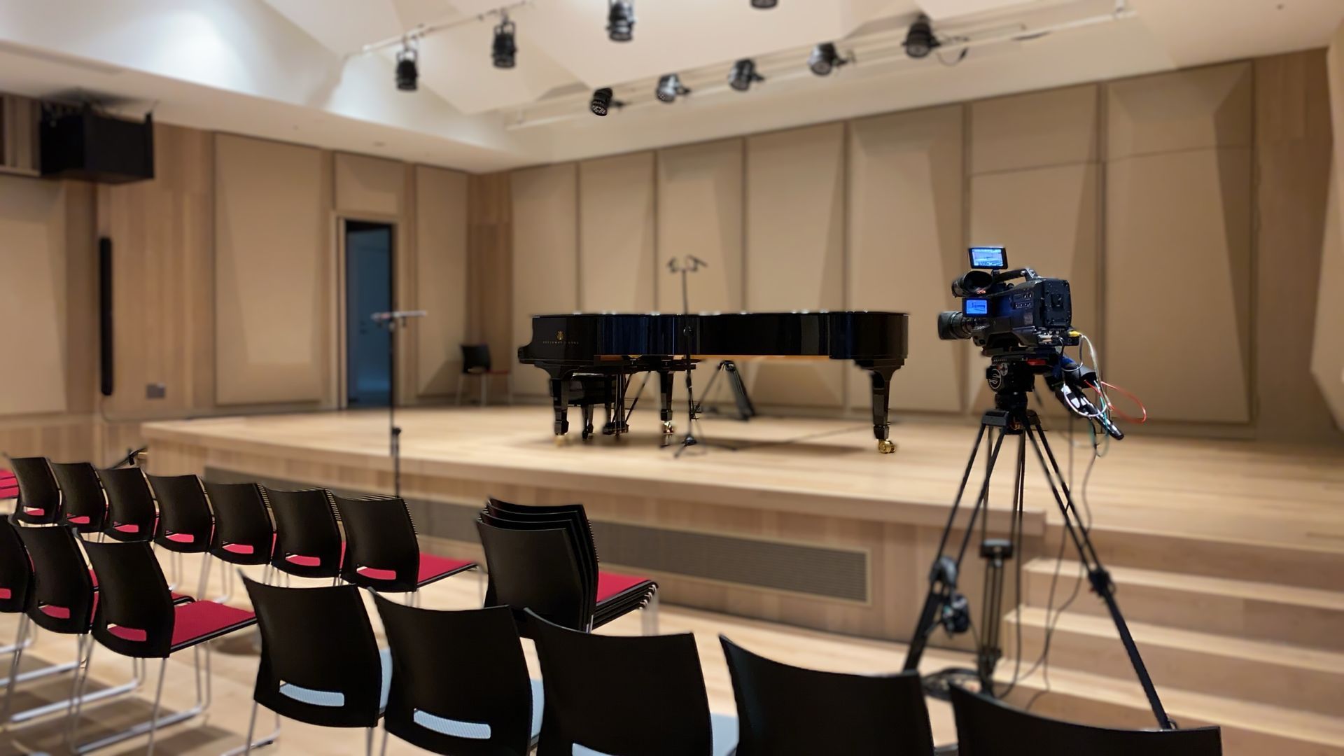 音樂廳舞台上有一架大鋼琴、一台三腳架上的攝影機和一排排座位。