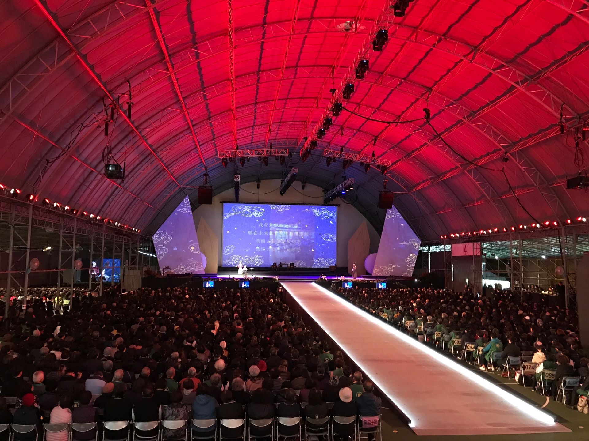 大型活動，有舞台、T 台和觀眾，在紅色燈光下。