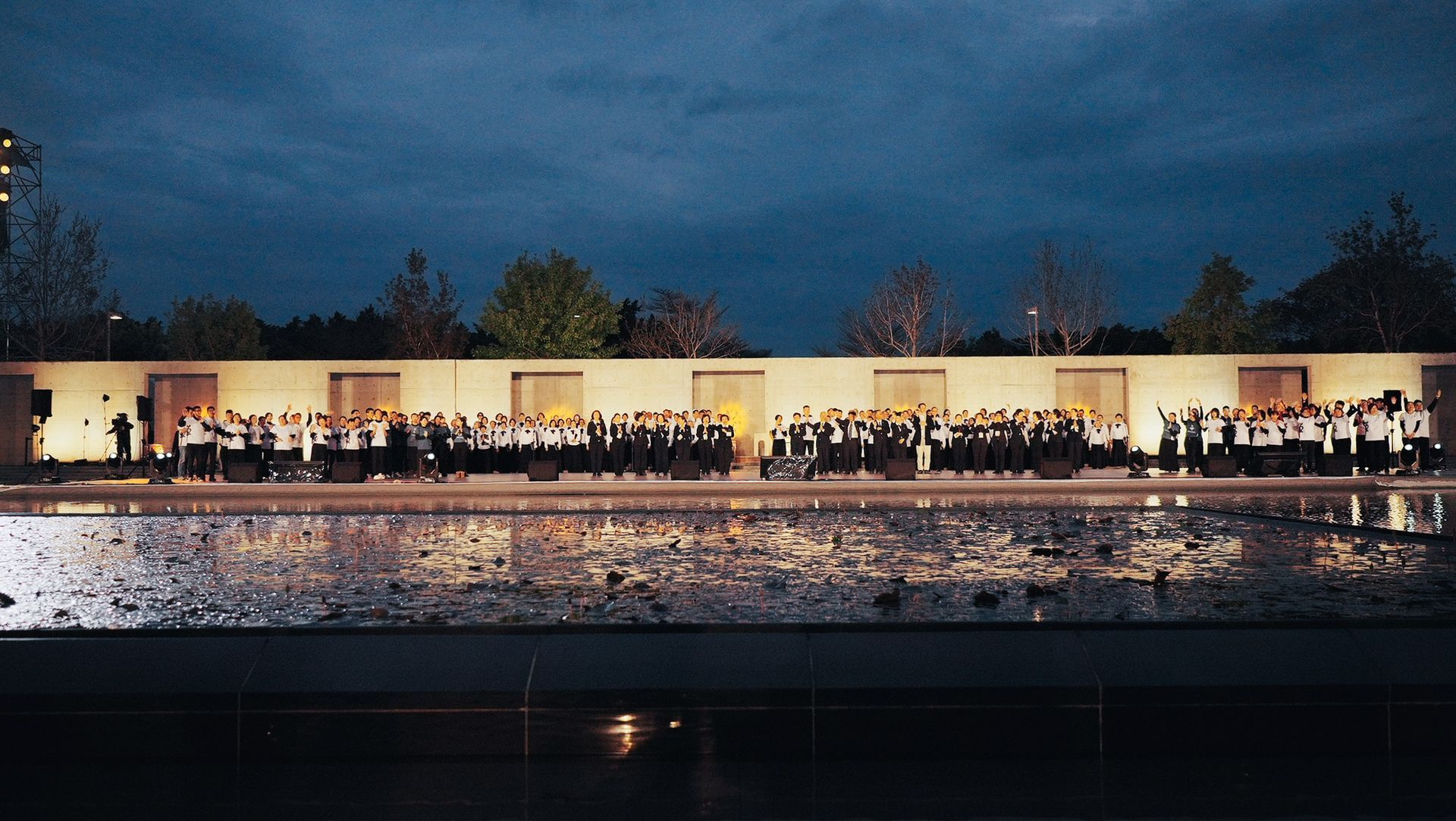 黃昏時分，一大群人站在水面上倒映的建築物前。