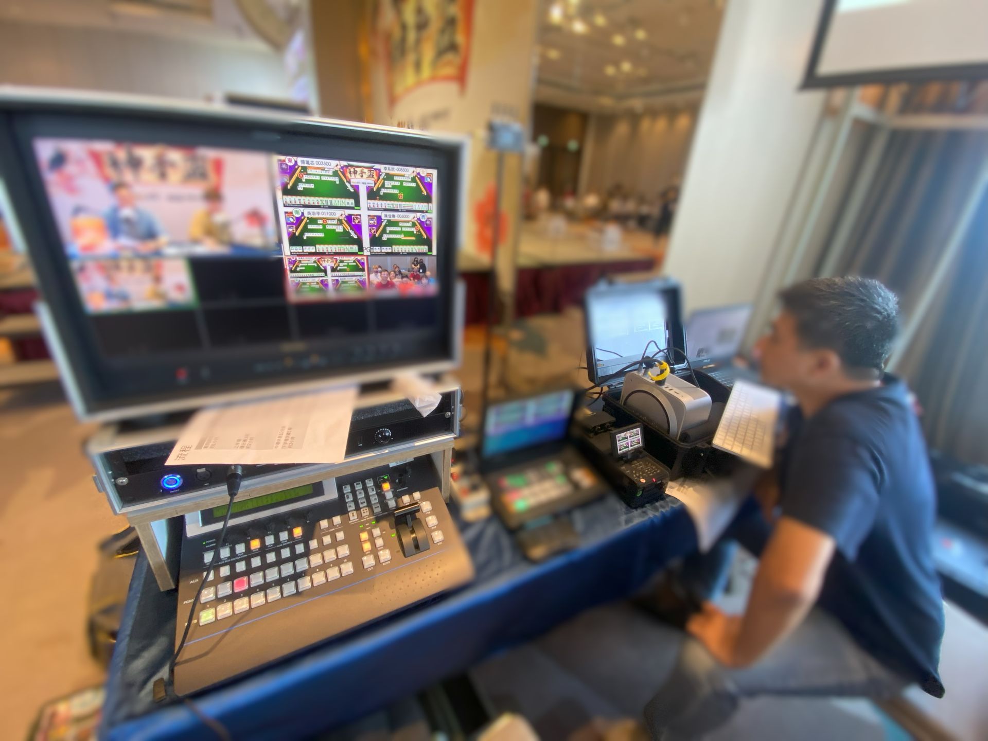 一名男子操作視訊設備，在會議環境中監控螢幕上的多個攝影機角度。