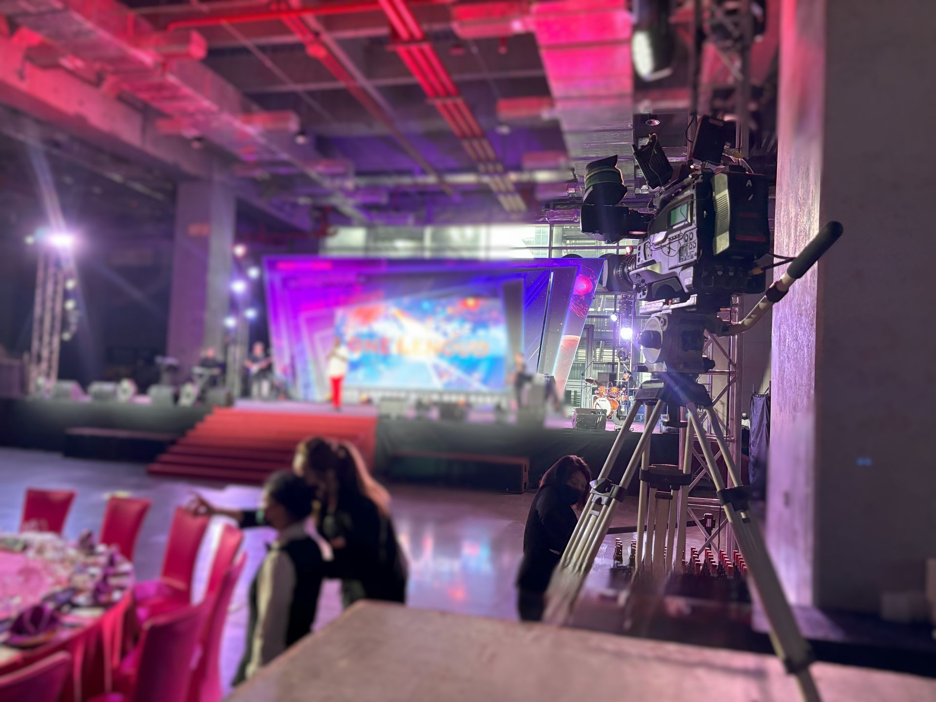 一台安裝在三腳架上的攝影機正在拍攝裝飾一新的宴會廳裡的舞台和在場的人們。
