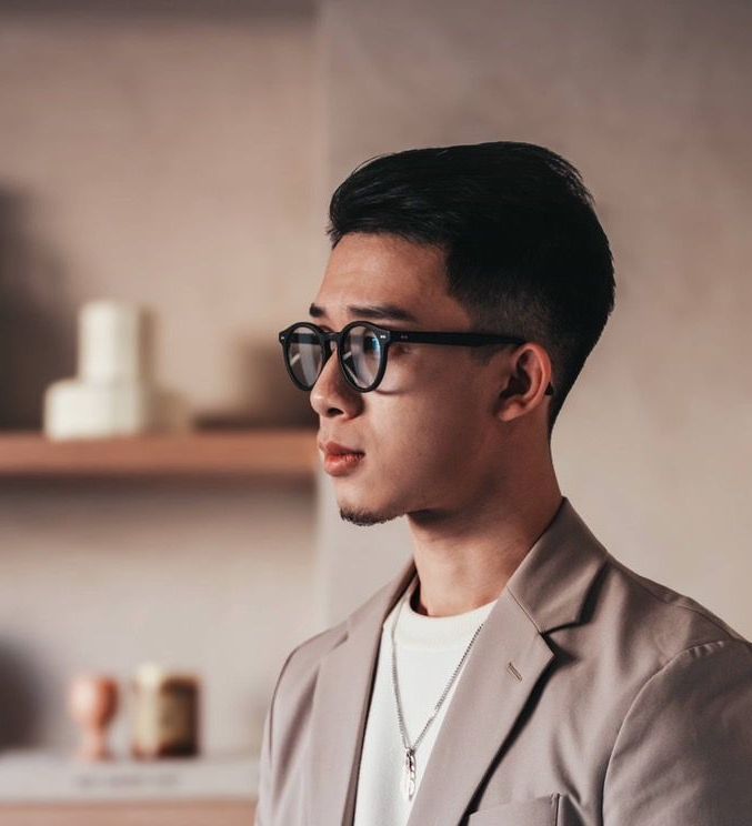 戴著眼鏡、穿著西裝的年輕人,看起來若有所思,背景中性。