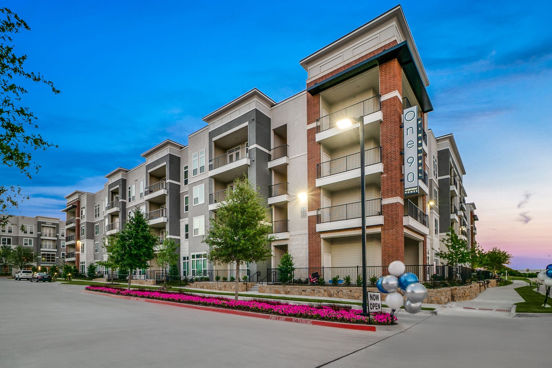 Exterior view of a modern apartment building with balconies and landscaped entry at dusk.