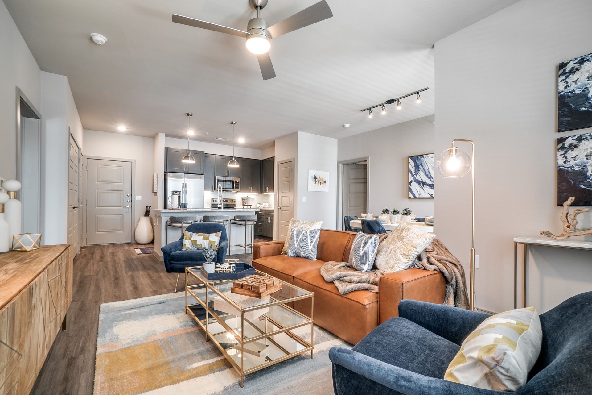 Open-concept living area with a kitchen island, sofa, and blue chairs in a modern apartment.