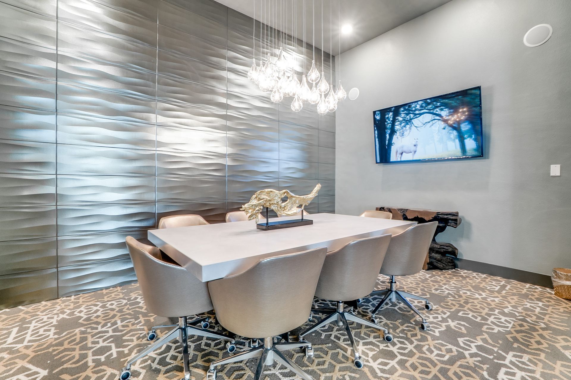 Modern community meeting room with textured wall panels, chandelier, and a wall-mounted TV.