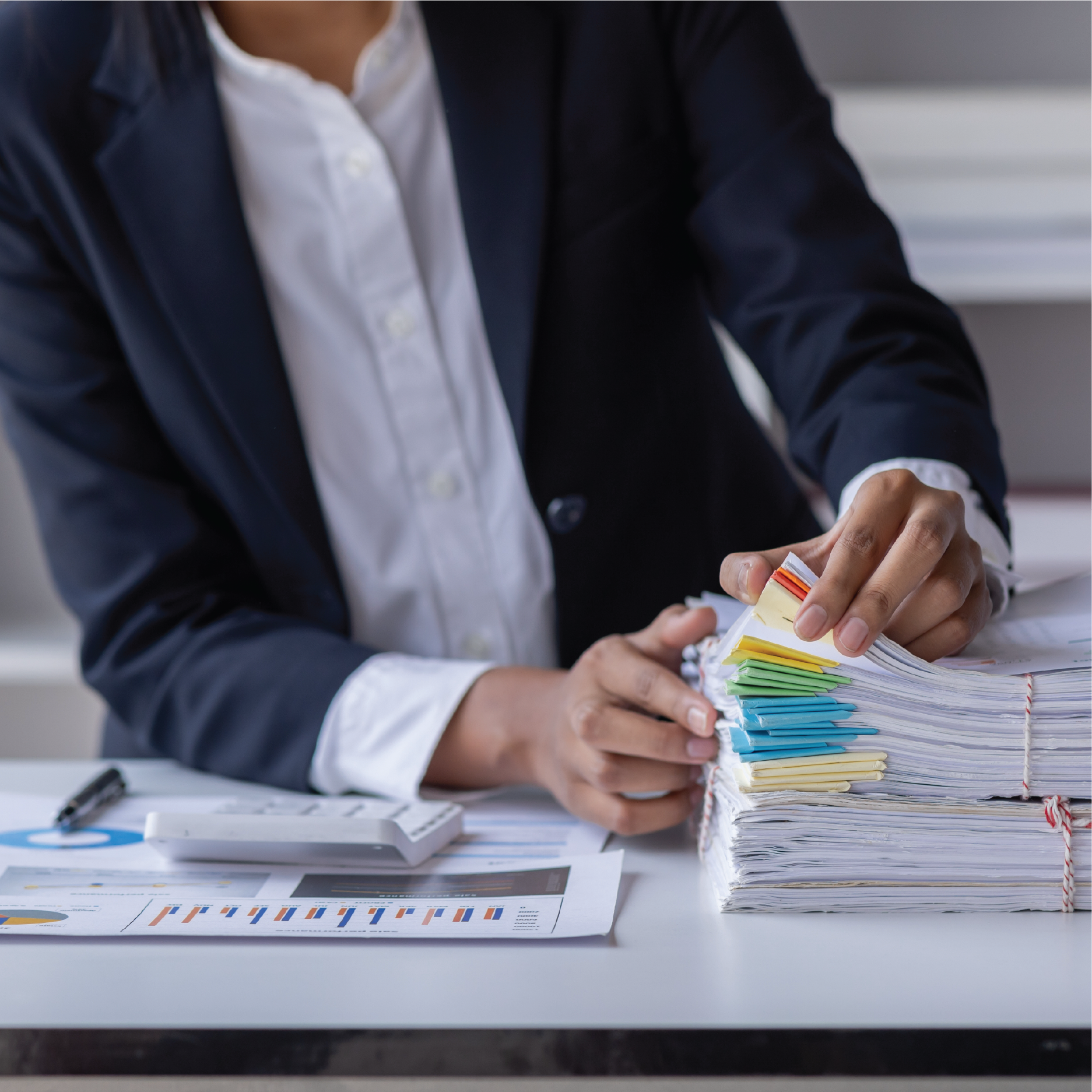 A woman is sitting at a desk with a stack of papers.