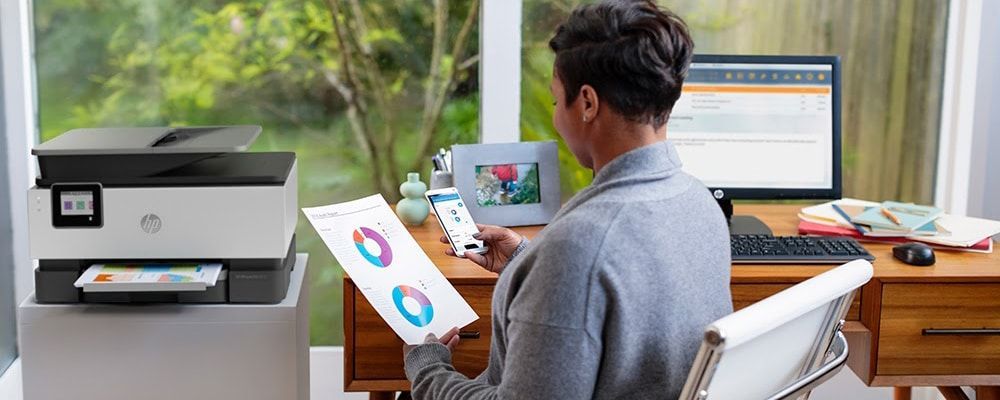 A man is sitting at a desk with a printer and a computer.