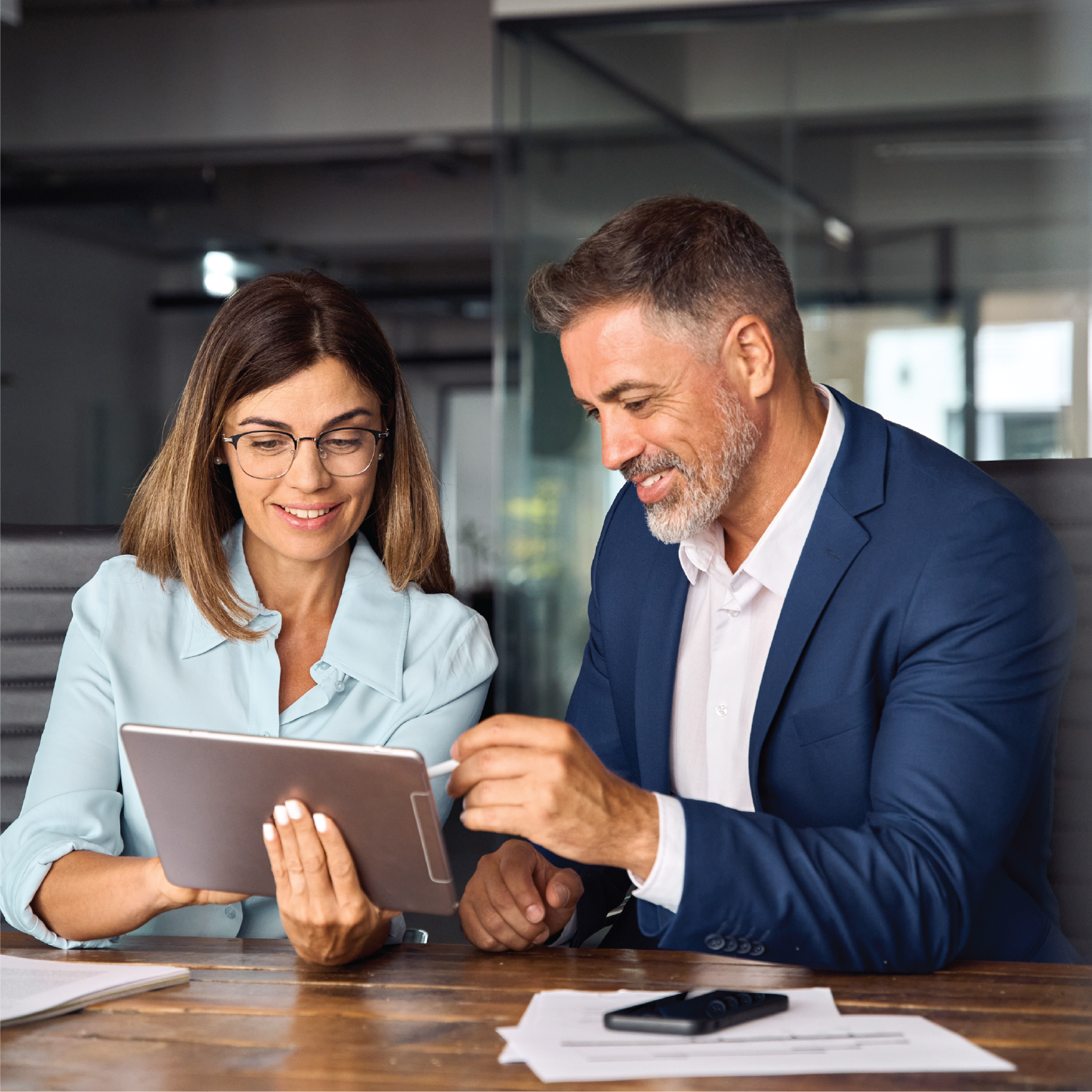 A man and a woman are sitting at a table looking at a tablet.