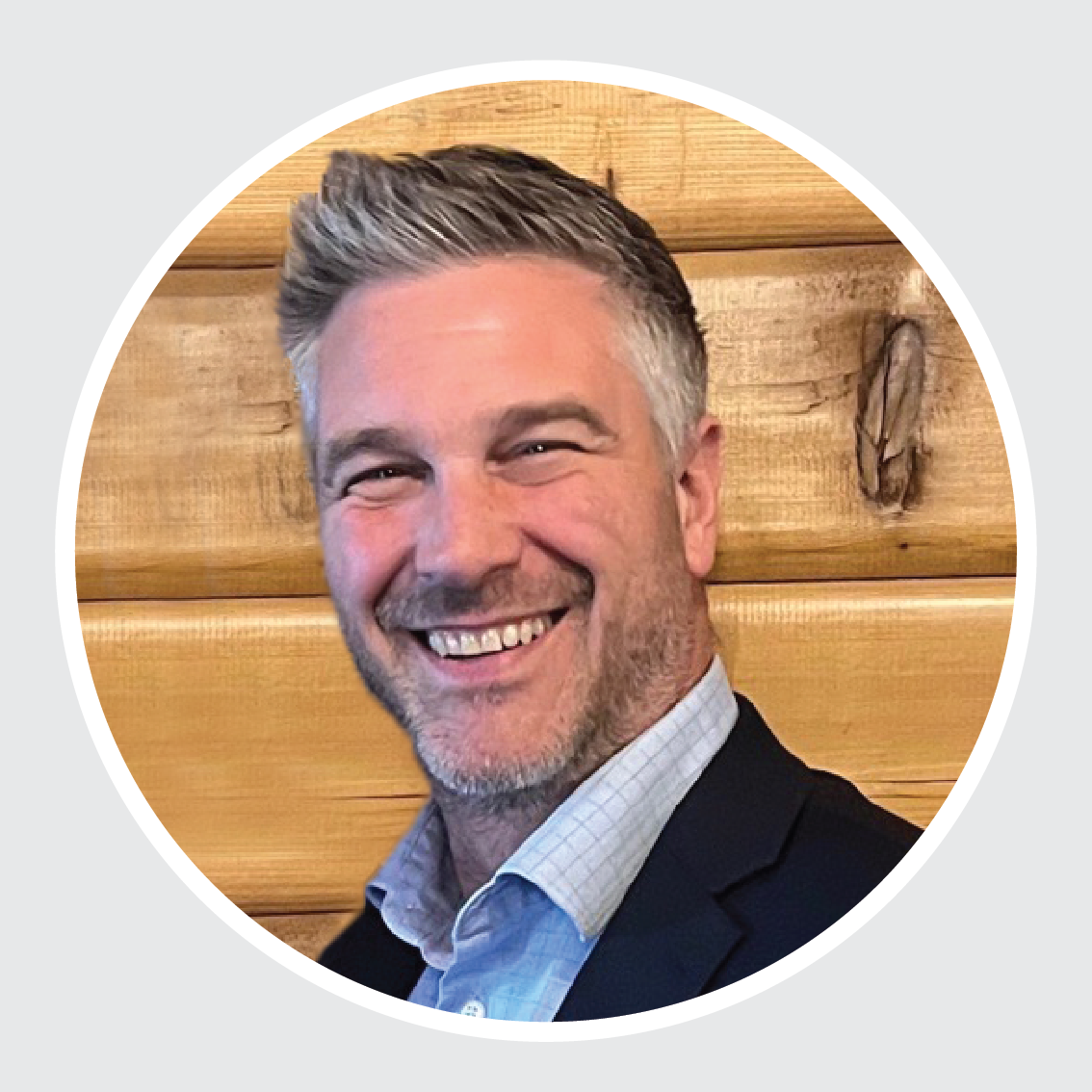 A man in a suit is smiling in front of a wooden wall.