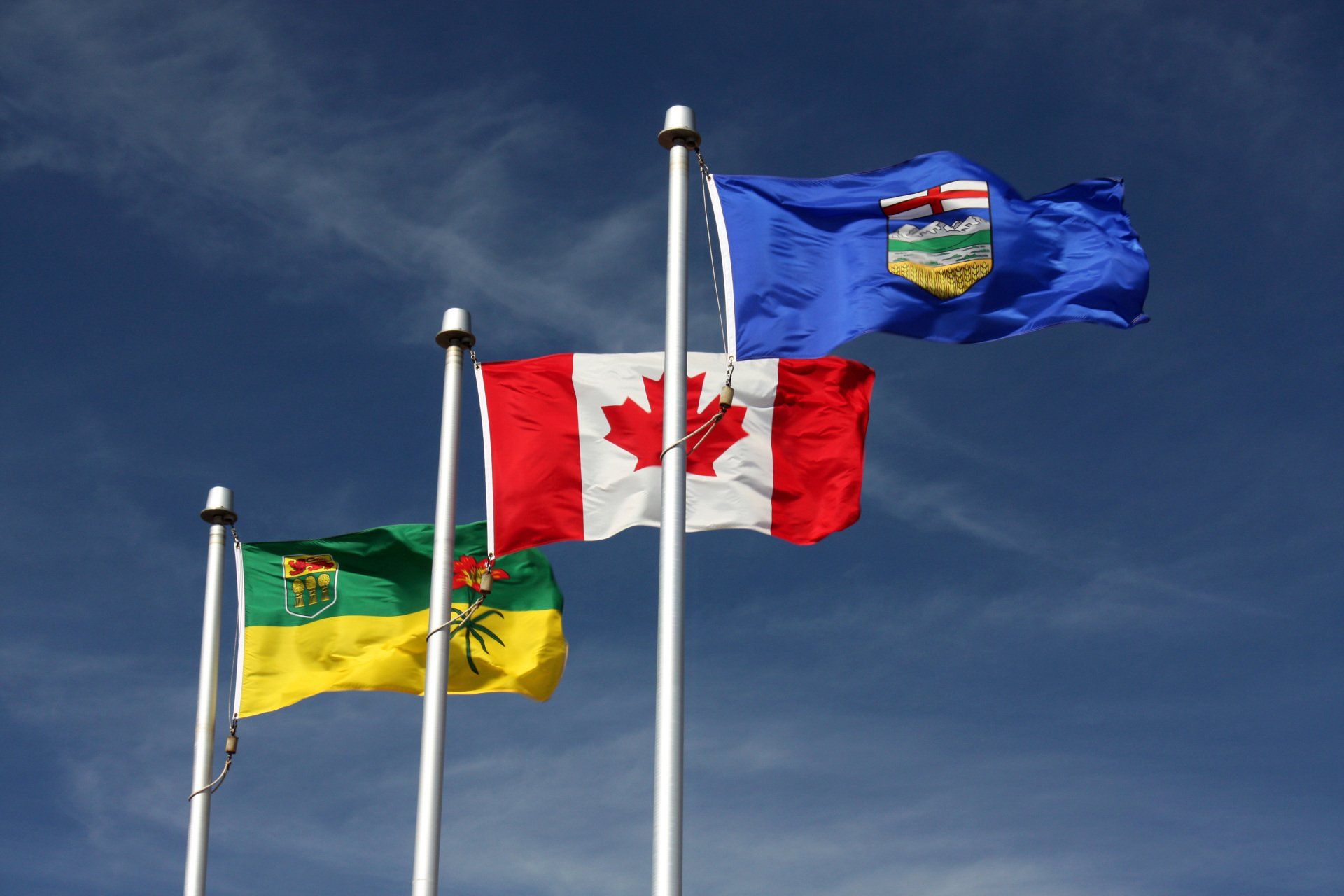 Three flags are waving in the wind including a canadian flag
