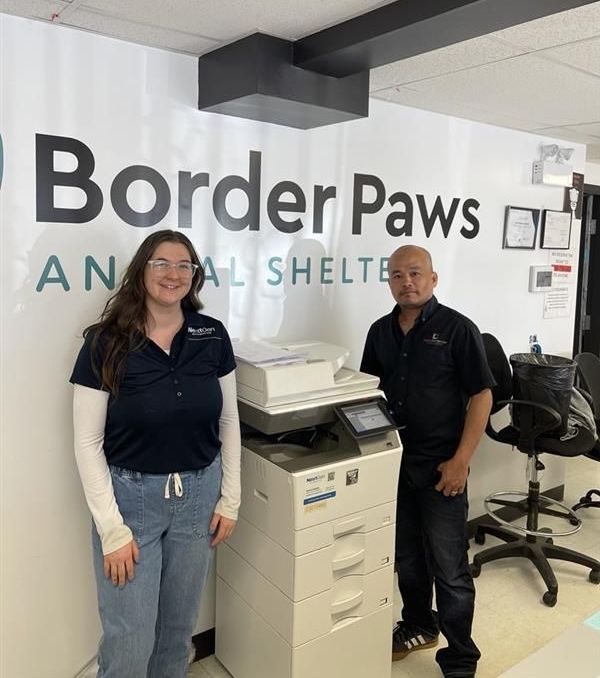 Two people standing in front of a sign that says border paws