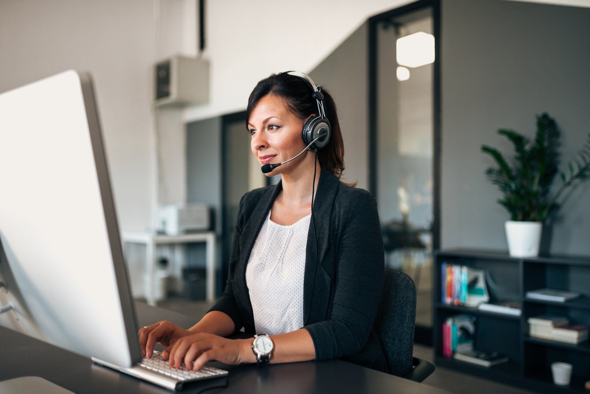 A woman wearing a headset is sitting in front of a computer.