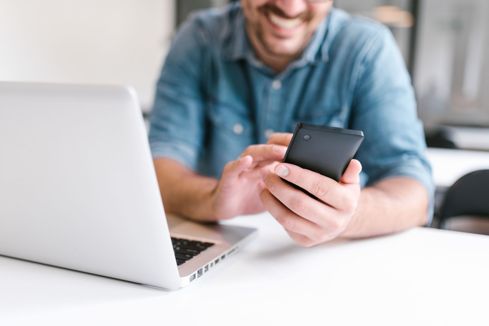A man is sitting at a table using a laptop and a cell phone.