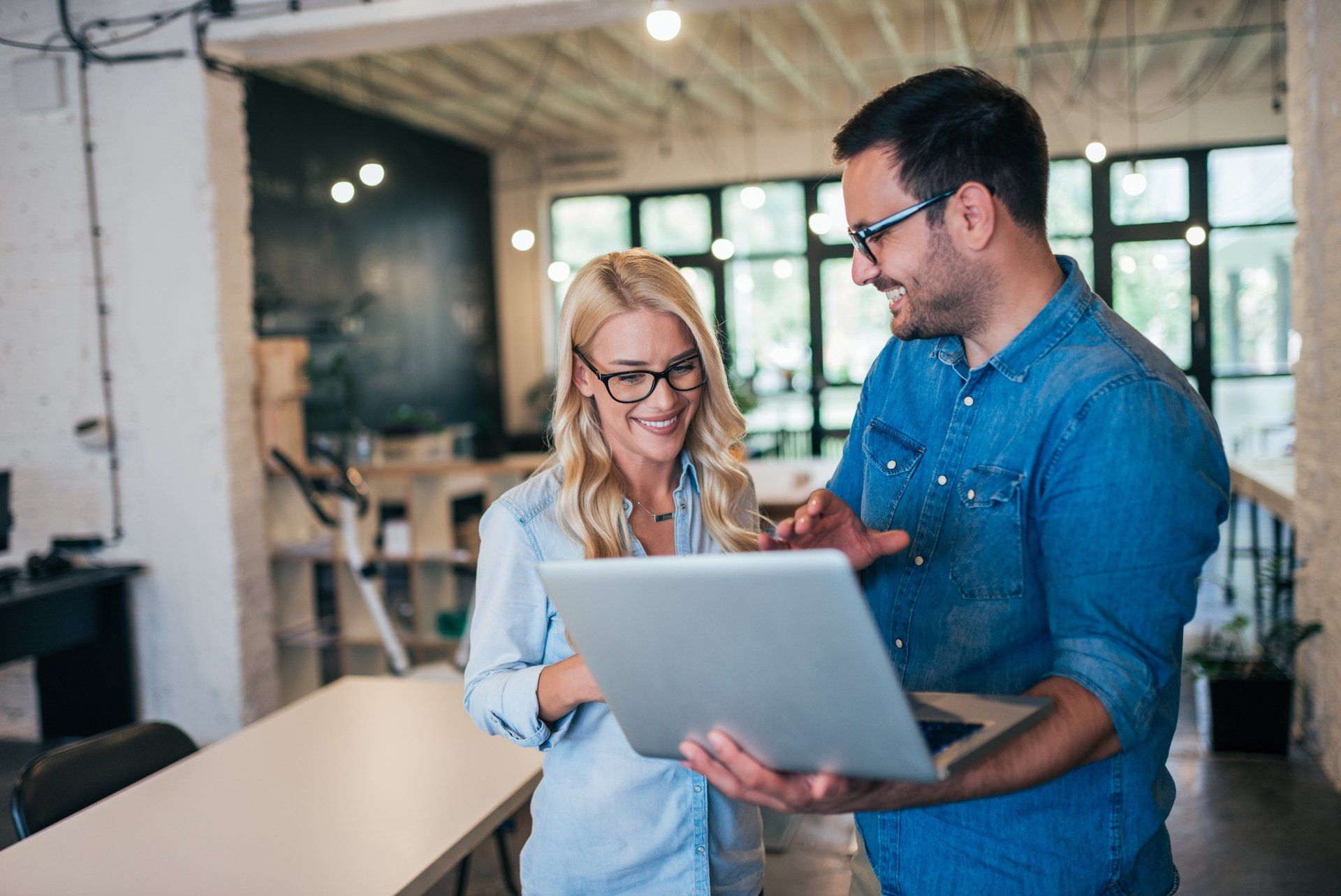 A man and a woman are looking at a laptop together in an office.