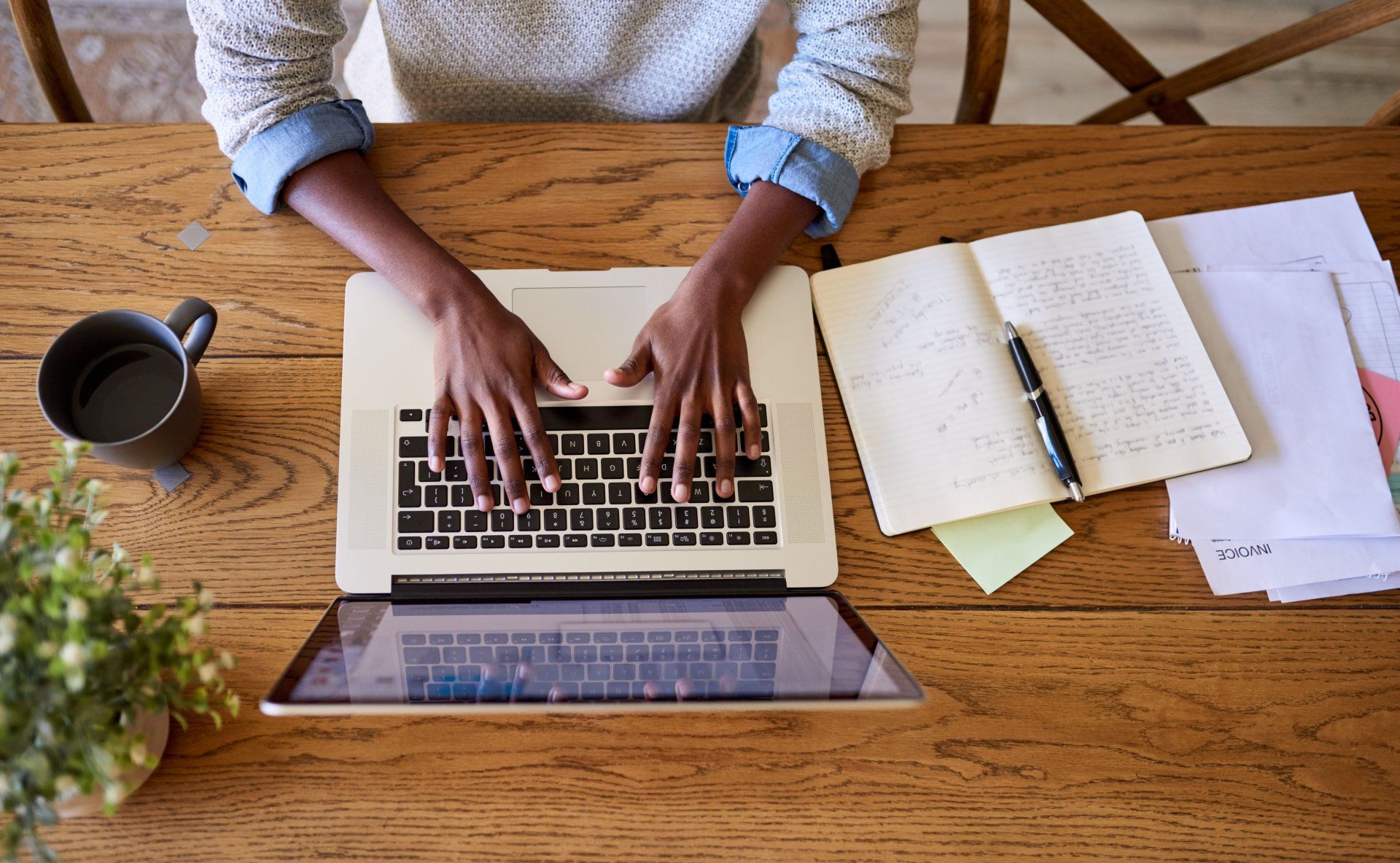 A person is typing on a laptop computer at a wooden desk.