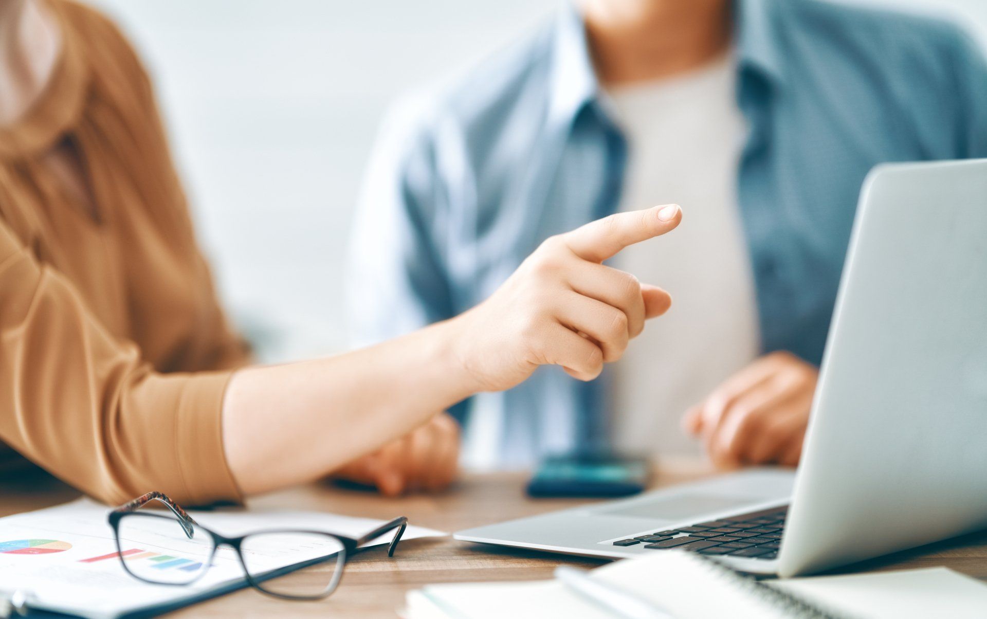 A man and a woman are sitting at a table looking at a laptop computer.