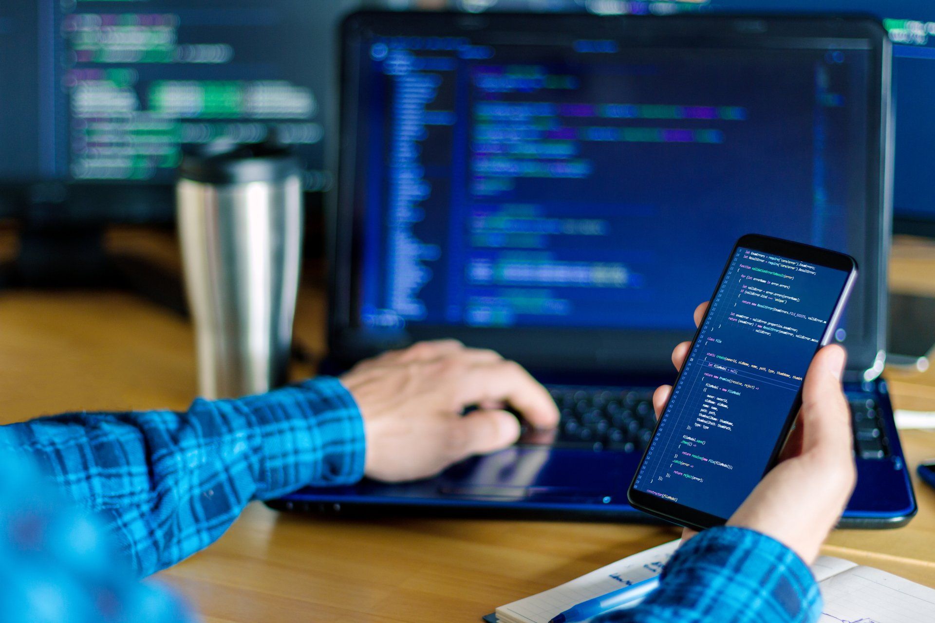 A person is holding a cell phone in front of a laptop computer.