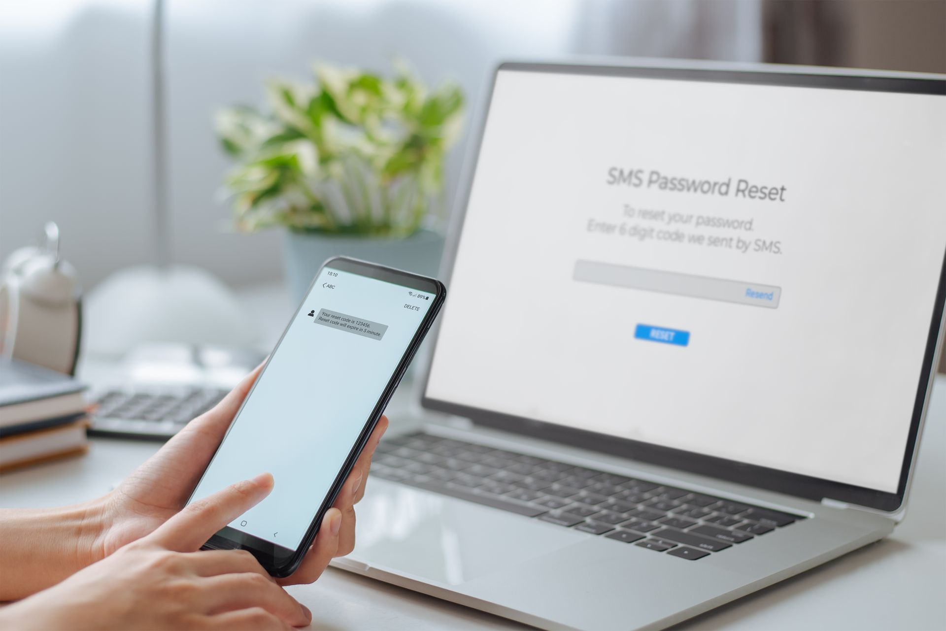 A person is holding a cell phone in front of a laptop computer.