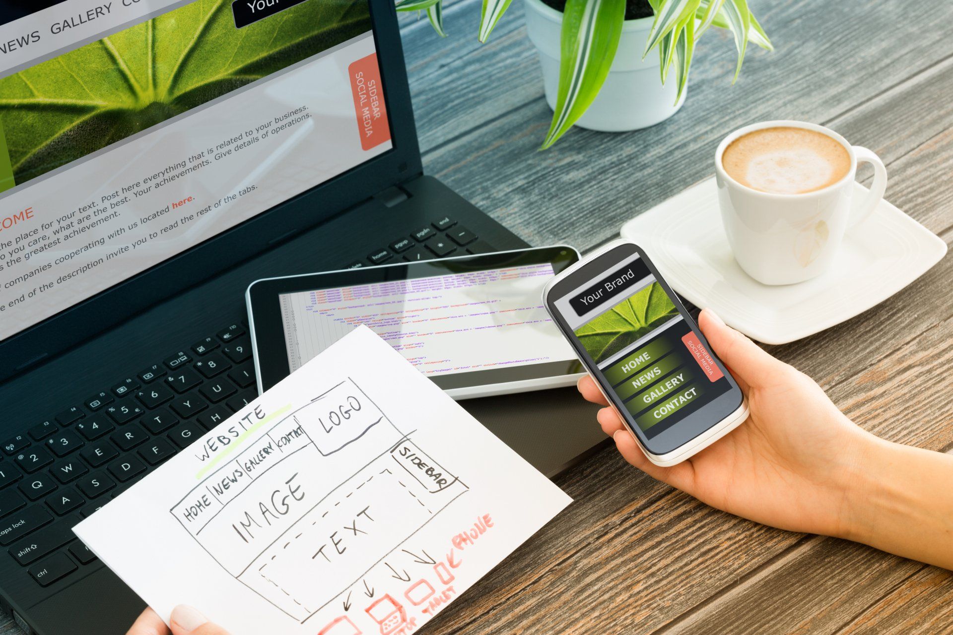 A person is holding a cell phone in front of a laptop.