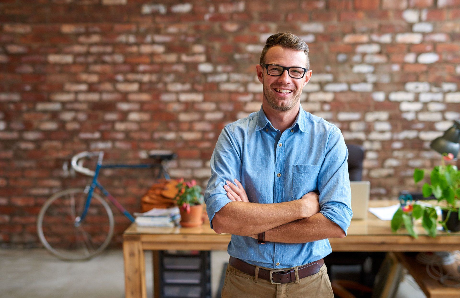 A man is standing in an office with his arms crossed and smiling.