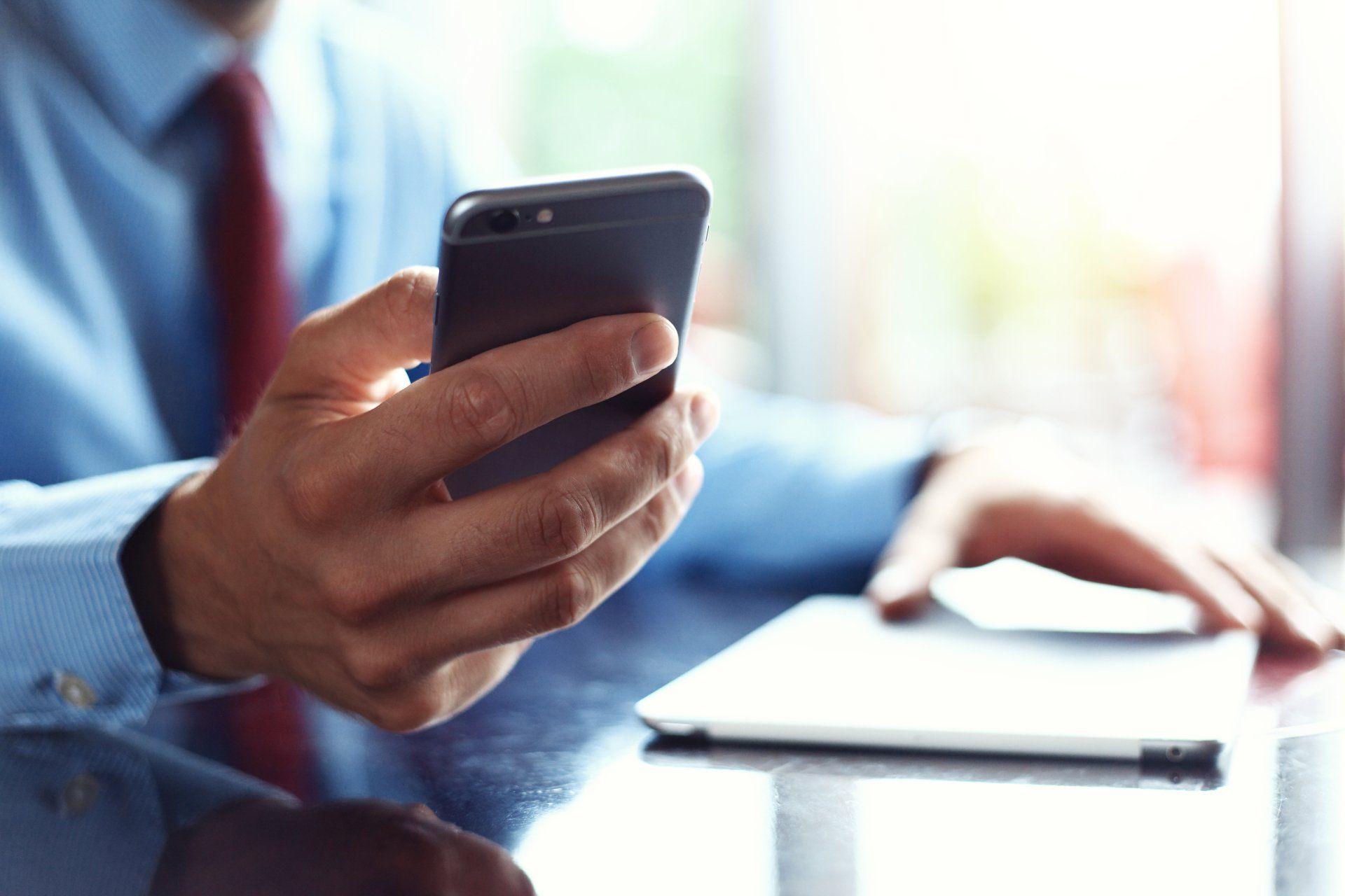 A man in a blue shirt and red tie is holding a cell phone in his hand.