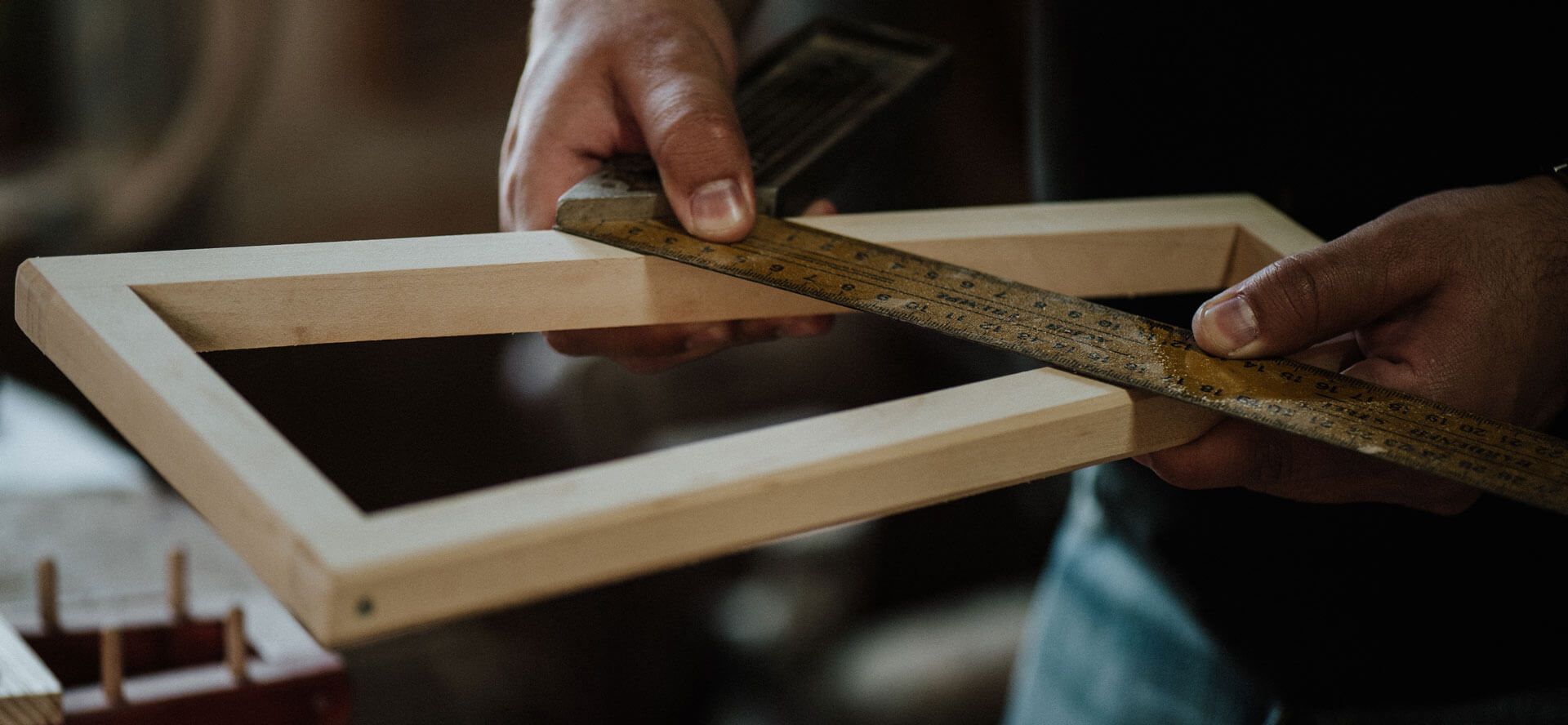 A person’s hands use a metal ruler to measure the corner of a wooden frame in a workshop.