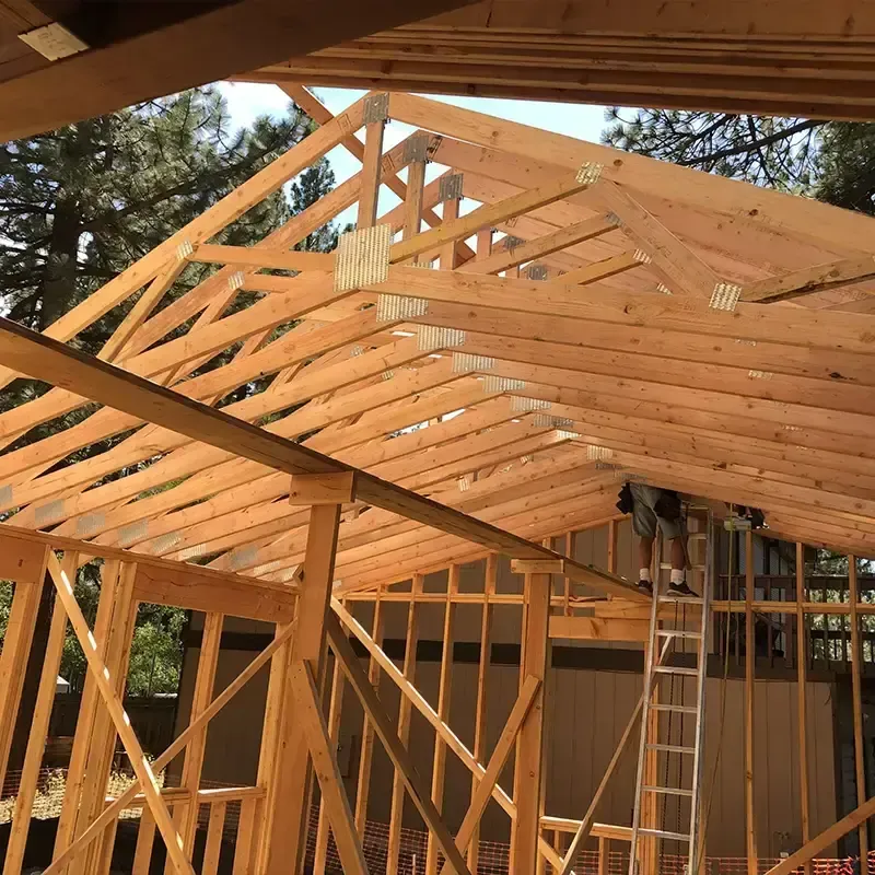Construction workers on a ladder installing wooden roof trusses for a building frame under trees.