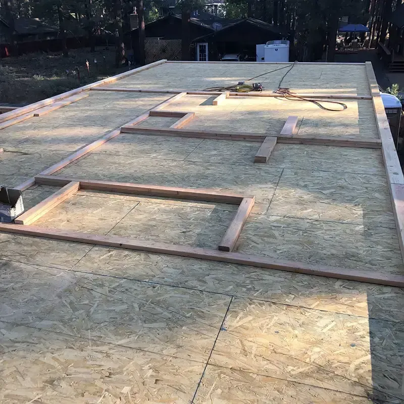 A construction site with wood framing for walls laid out on a flat, plywood subfloor foundation in an outdoor setting.