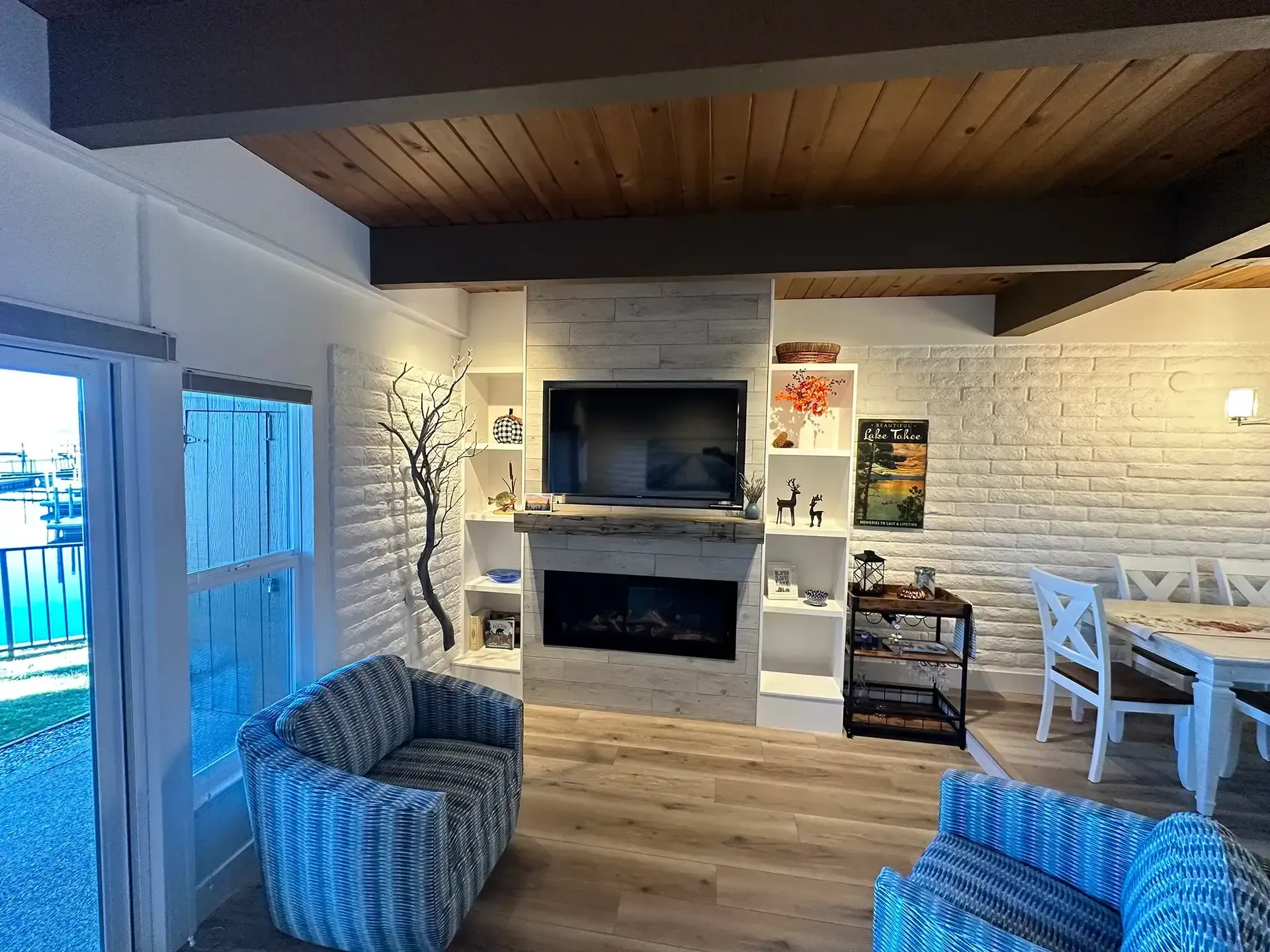 A living room features a TV above a fireplace, two blue patterned chairs, and a dining table with white chairs.
