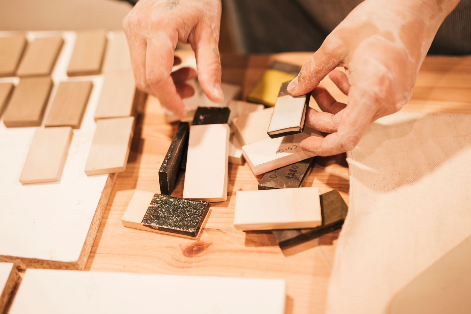 Hands sorting small rectangular material samples of various colors and textures on a wooden workspace.