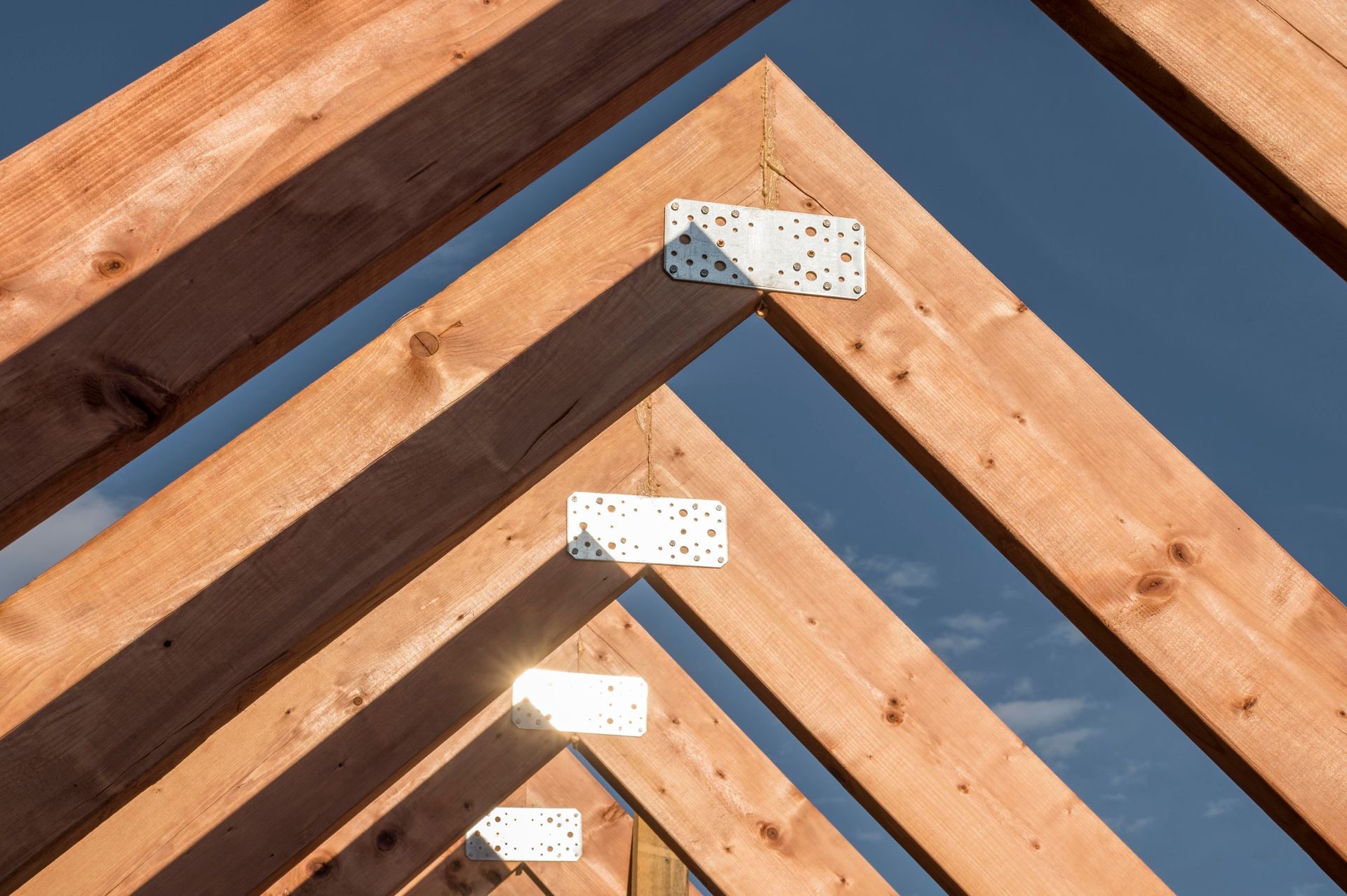 Wooden roof trusses connected by metal plates set against a clear blue sky.