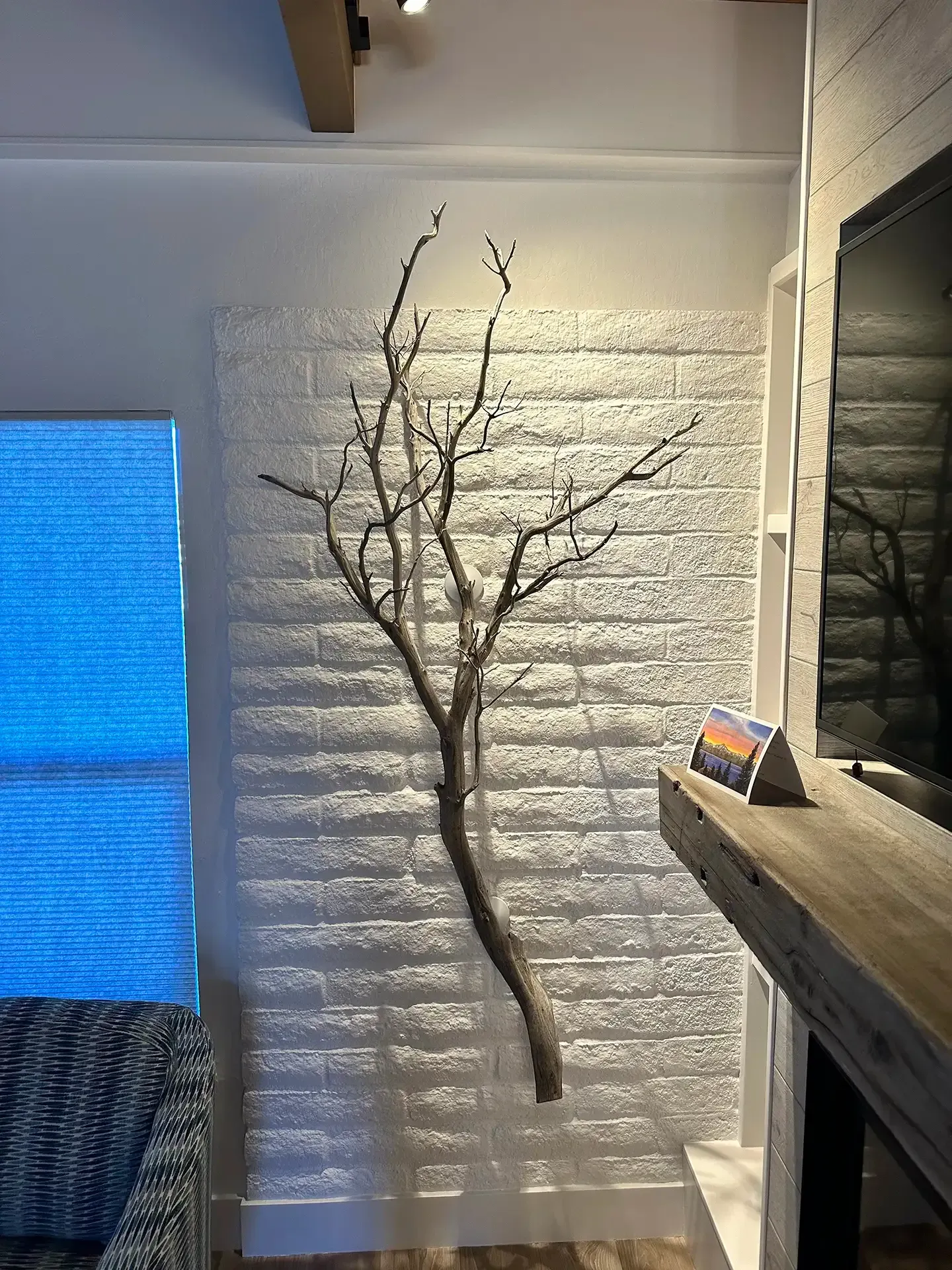 A large, natural, bare tree branch mounted vertically on a white painted brick wall next to a fireplace mantel.