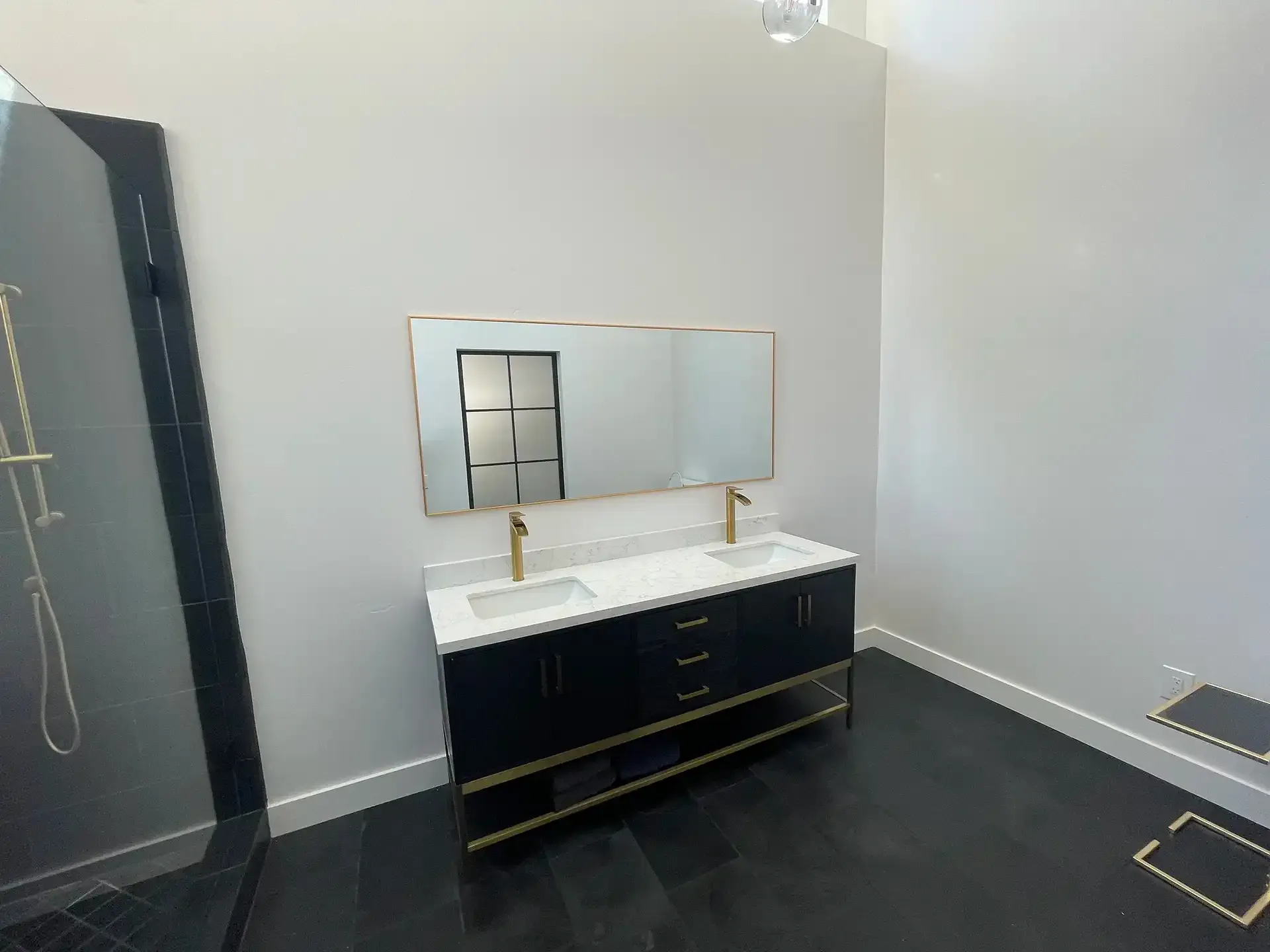 A modern bathroom featuring a black double vanity with gold accents, matching gold faucets, and a wide rectangular mirror.