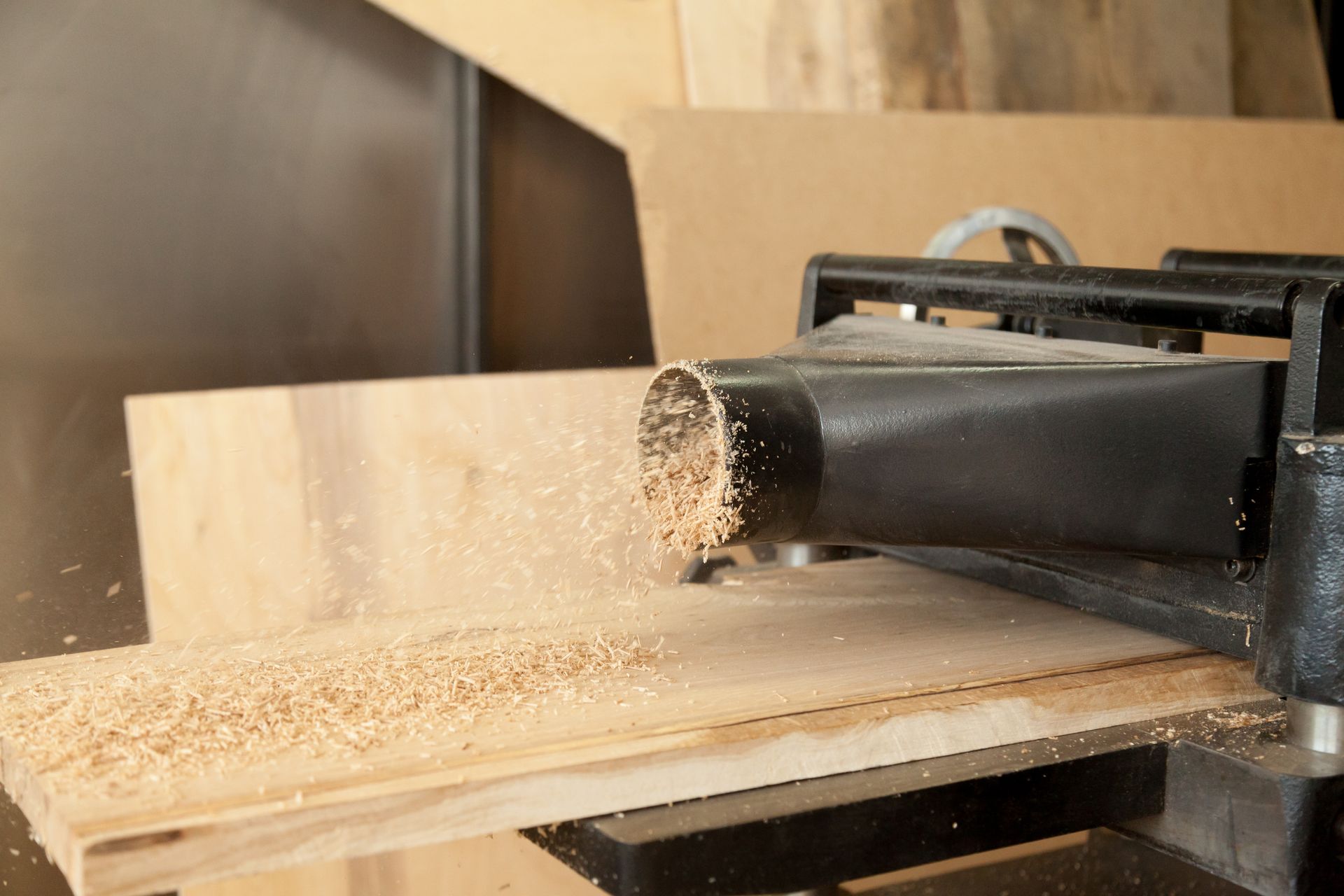 A wood planer in a workshop shaving sawdust off a wooden board.
