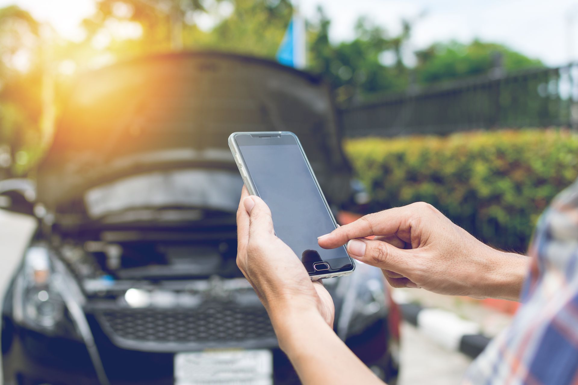 Person using a smartphone in front of an open car hood, checking vehicle issue outdoors. Person using a smartphone in front of an open car hood, checking vehicle issue outdoors.