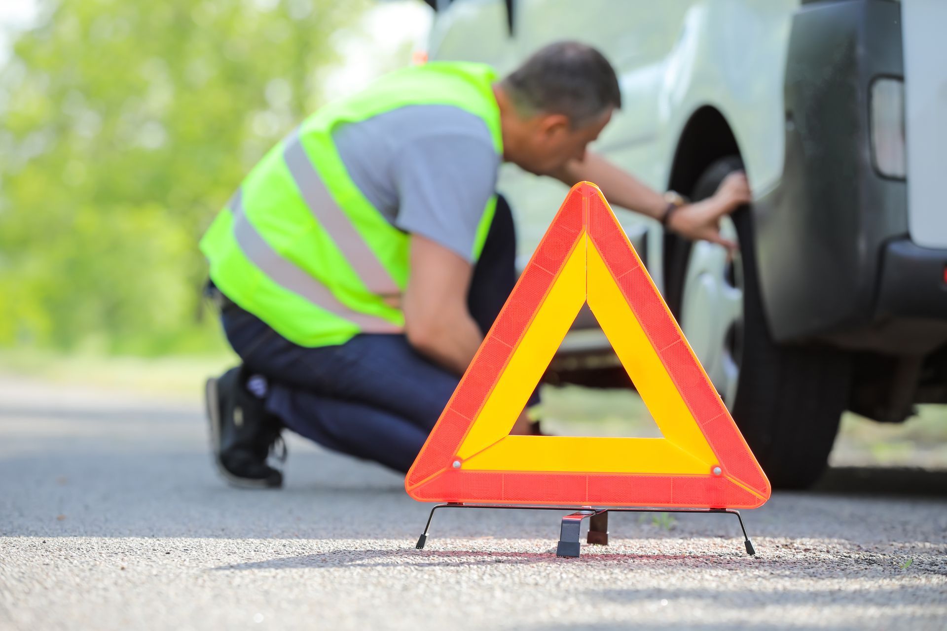 Warning triangle on road as person checks a vehicle tire during roadside breakdown. Warning triangle on road as person checks a vehicle tire during roadside breakdown.