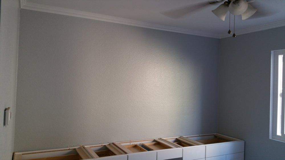 A light gray room with white crown molding. Built-in, unfinished cabinets are along the bottom.