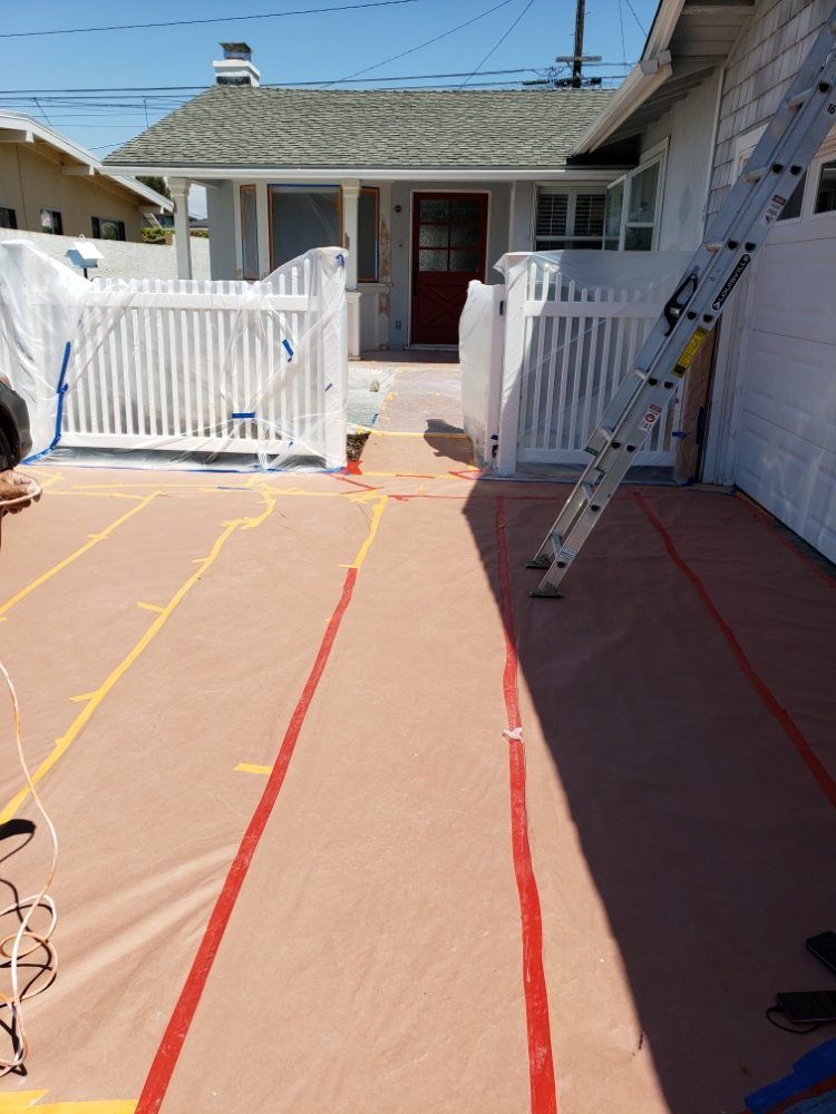 House exterior being painted, covered with plastic sheeting and marked with tape. White picket fence, red door.