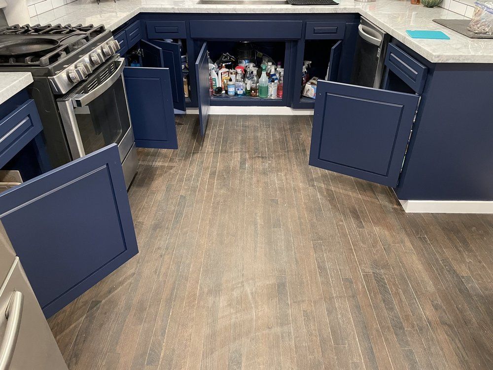 Kitchen with blue cabinets, open doors, stainless steel appliances, and wood-look flooring.