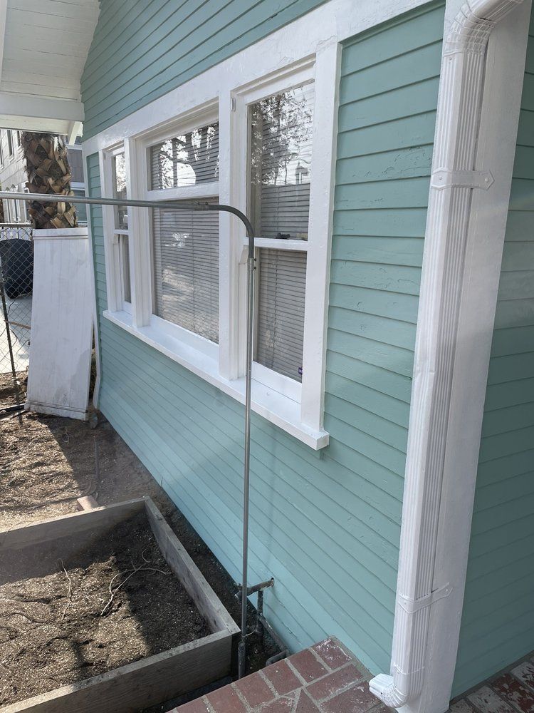 Side view of a house with teal siding, white trim, and a raised garden bed.