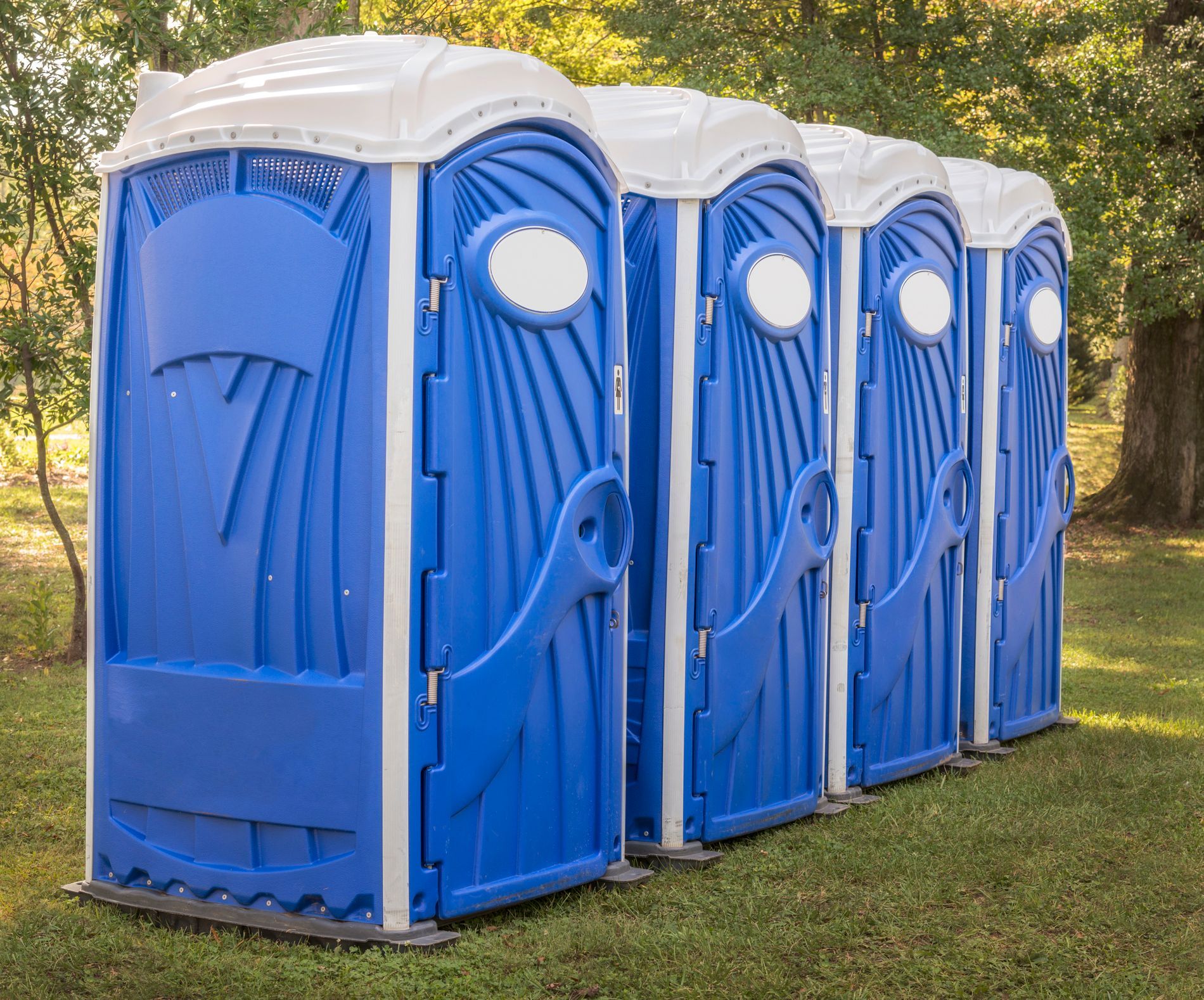 A blue portable toilet is sitting in the middle of a grassy field.