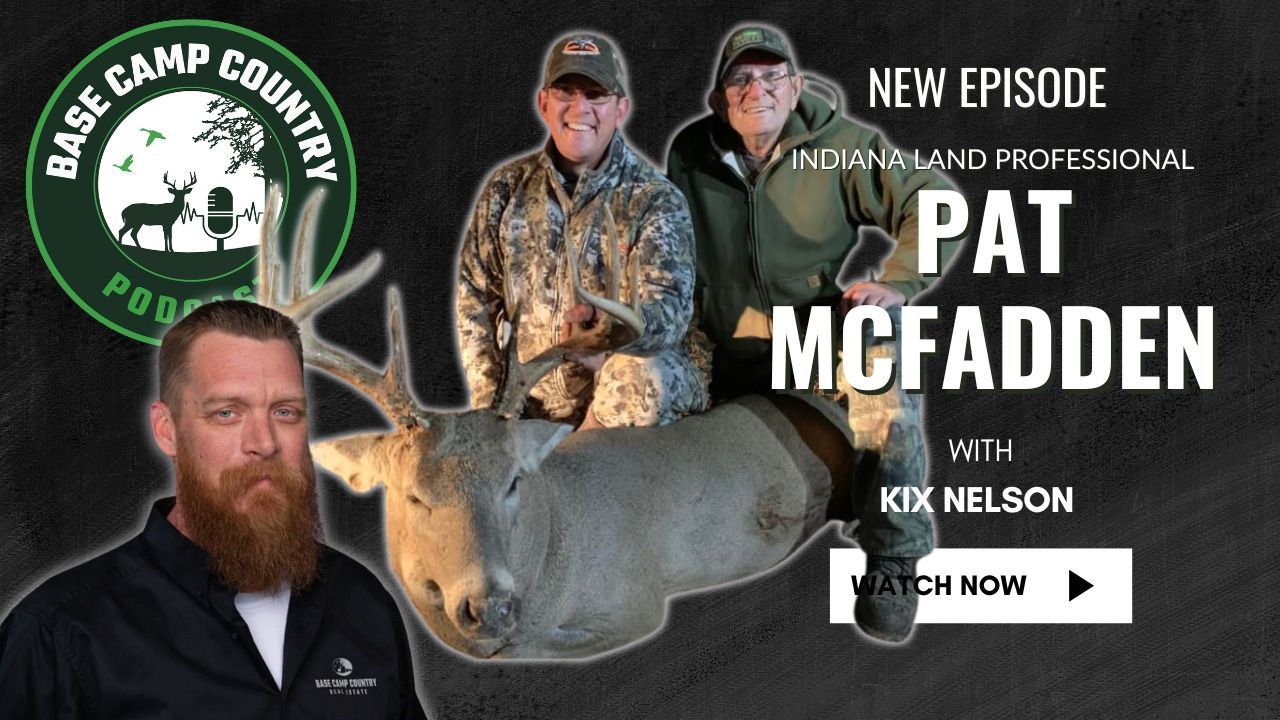 A man with a beard is holding a deer in front of a sign that says pat mcfadden