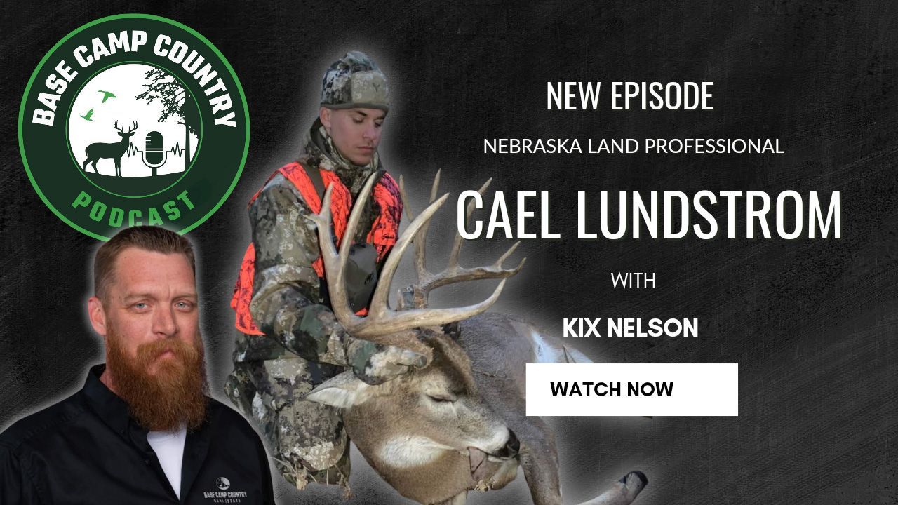 A man with a beard is holding a deer in front of a sign that says base camp country podcast