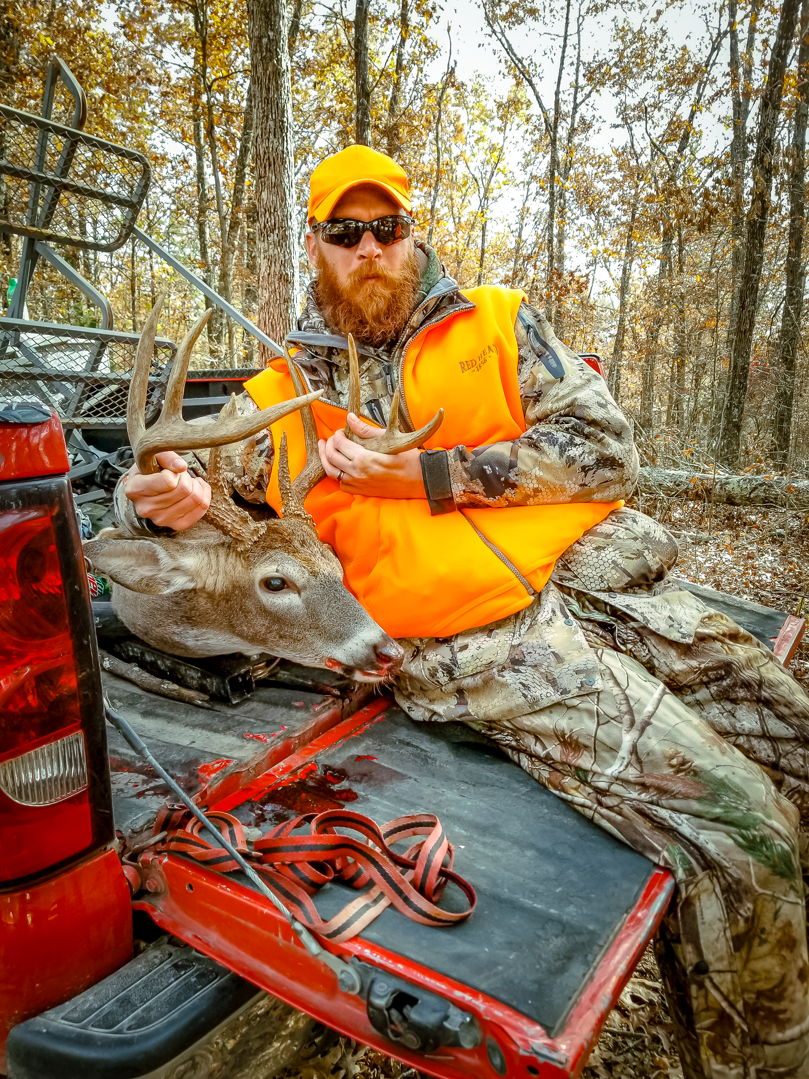 A man is sitting in the back of a truck holding antlers.